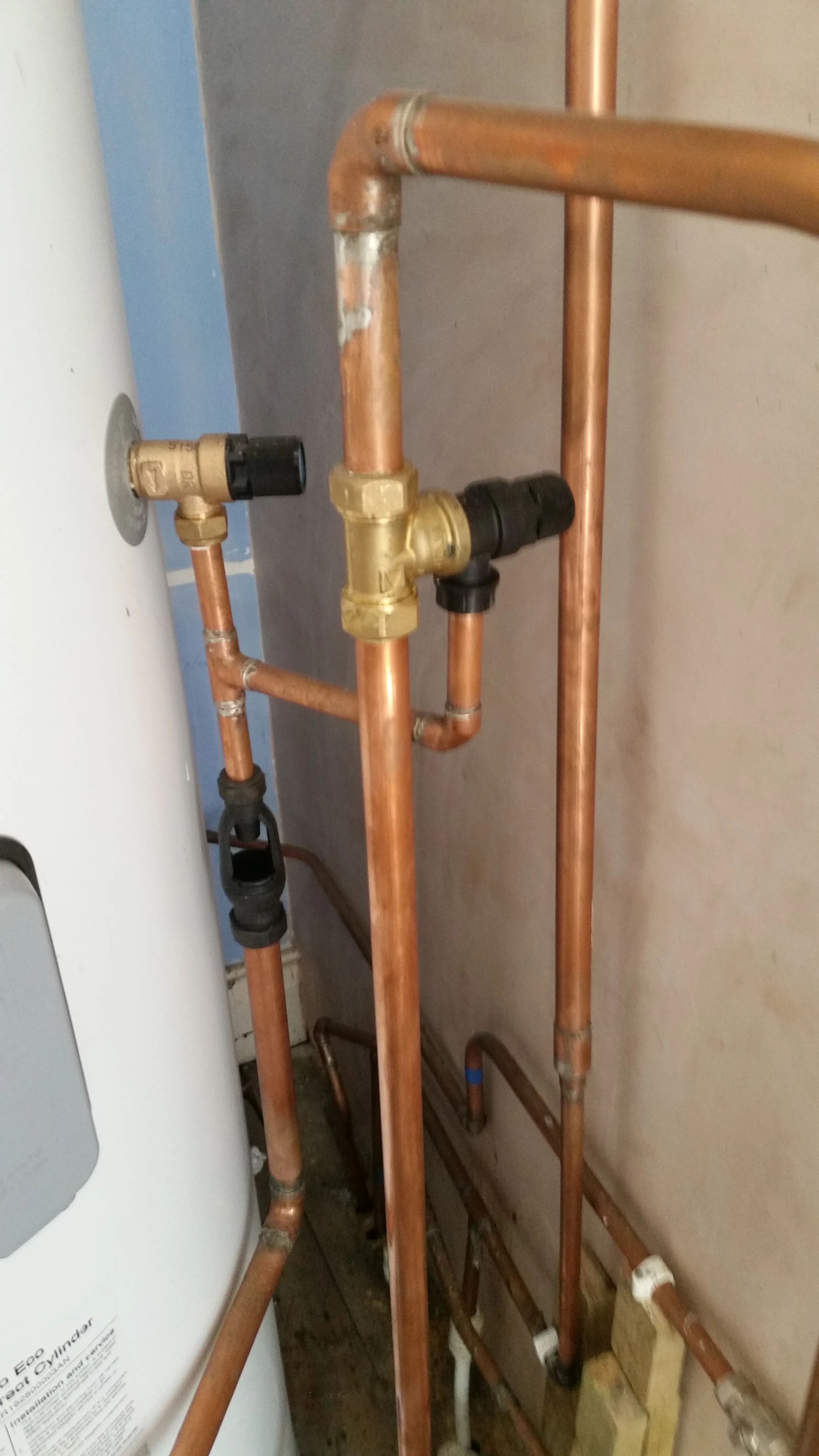 Close-up of copper plumbing pipes and brass valves connected to a white hot water cylinder.