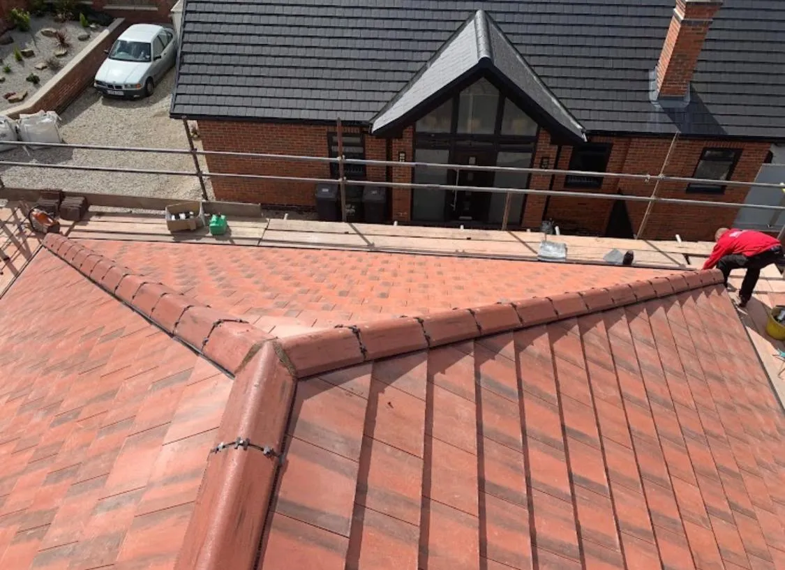 Newly installed pitched roof with red-brown tiles and a roofer working on site.