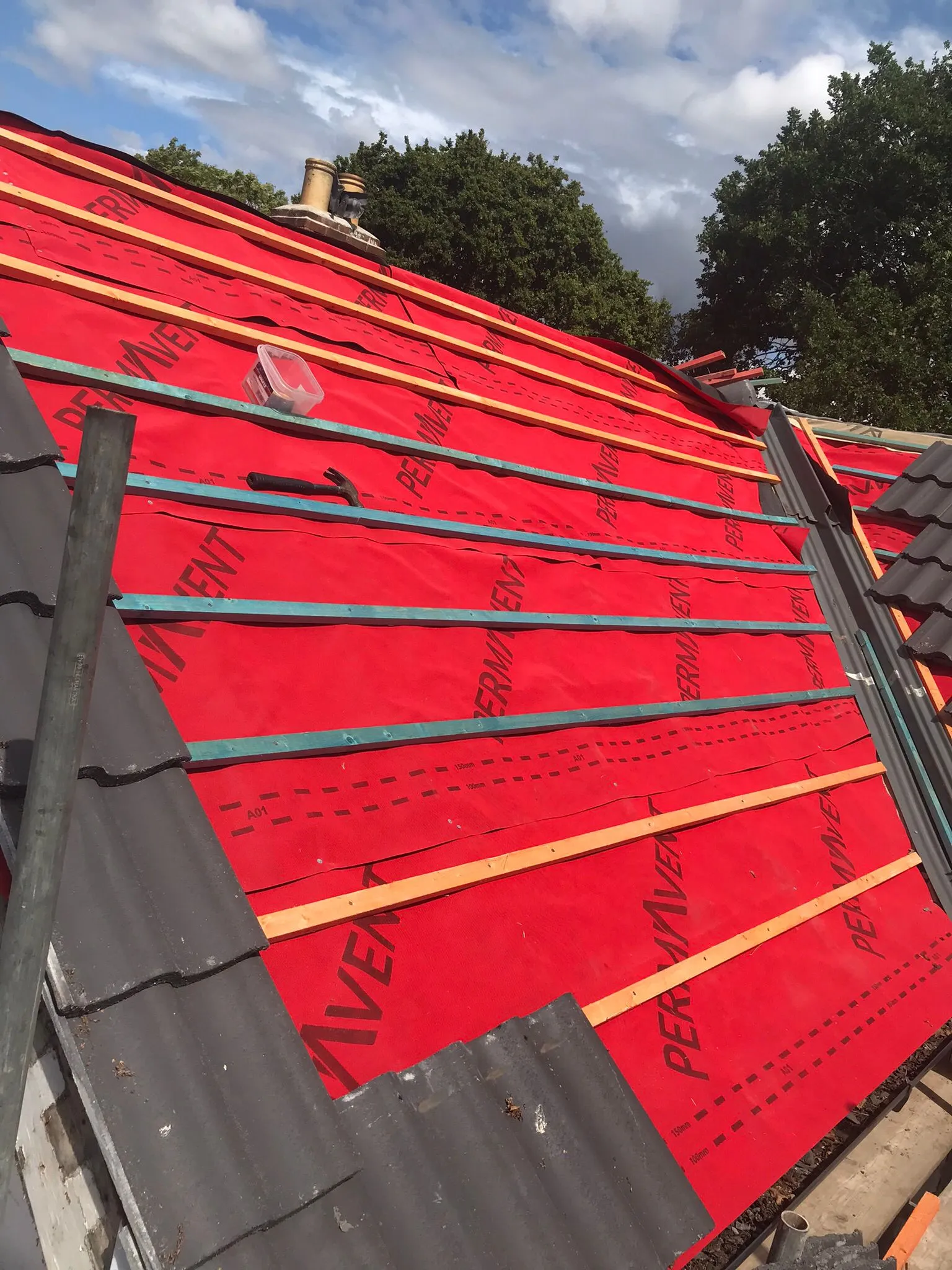 Pitched roof installation in progress with red underlayment and new tiles