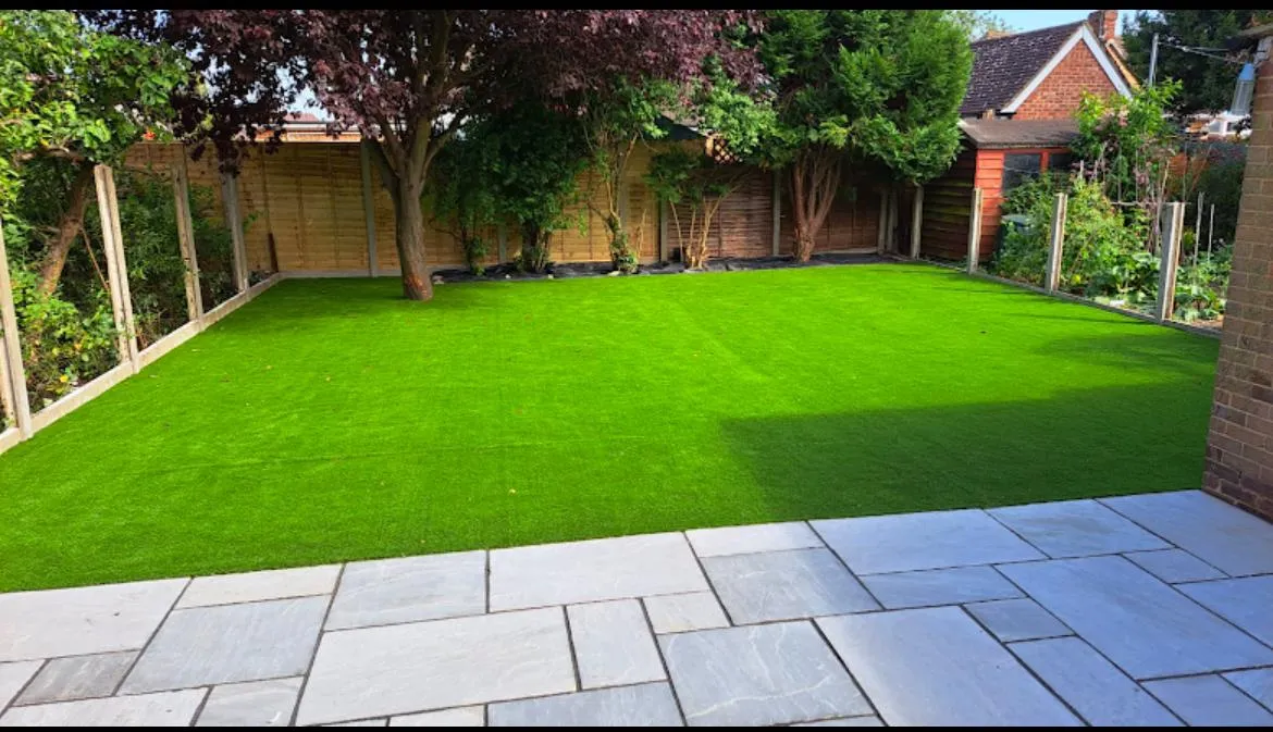 A newly landscaped garden with a light grey patio, a bright green artificial turf lawn, and new timber fencing.