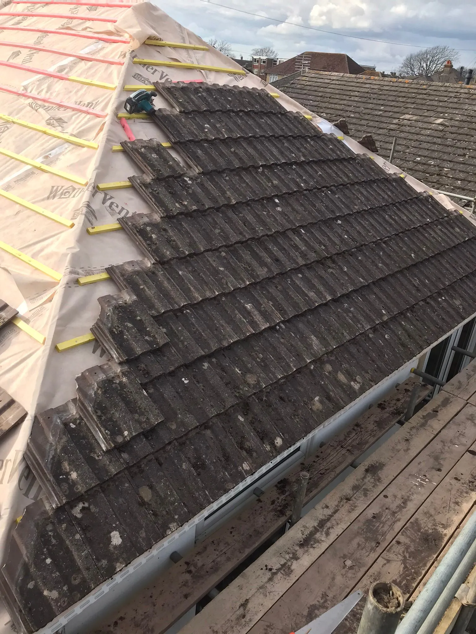 Roof renovation in progress on a residential property, with old roof tiles contrasting with new underlayment and wooden battens.
