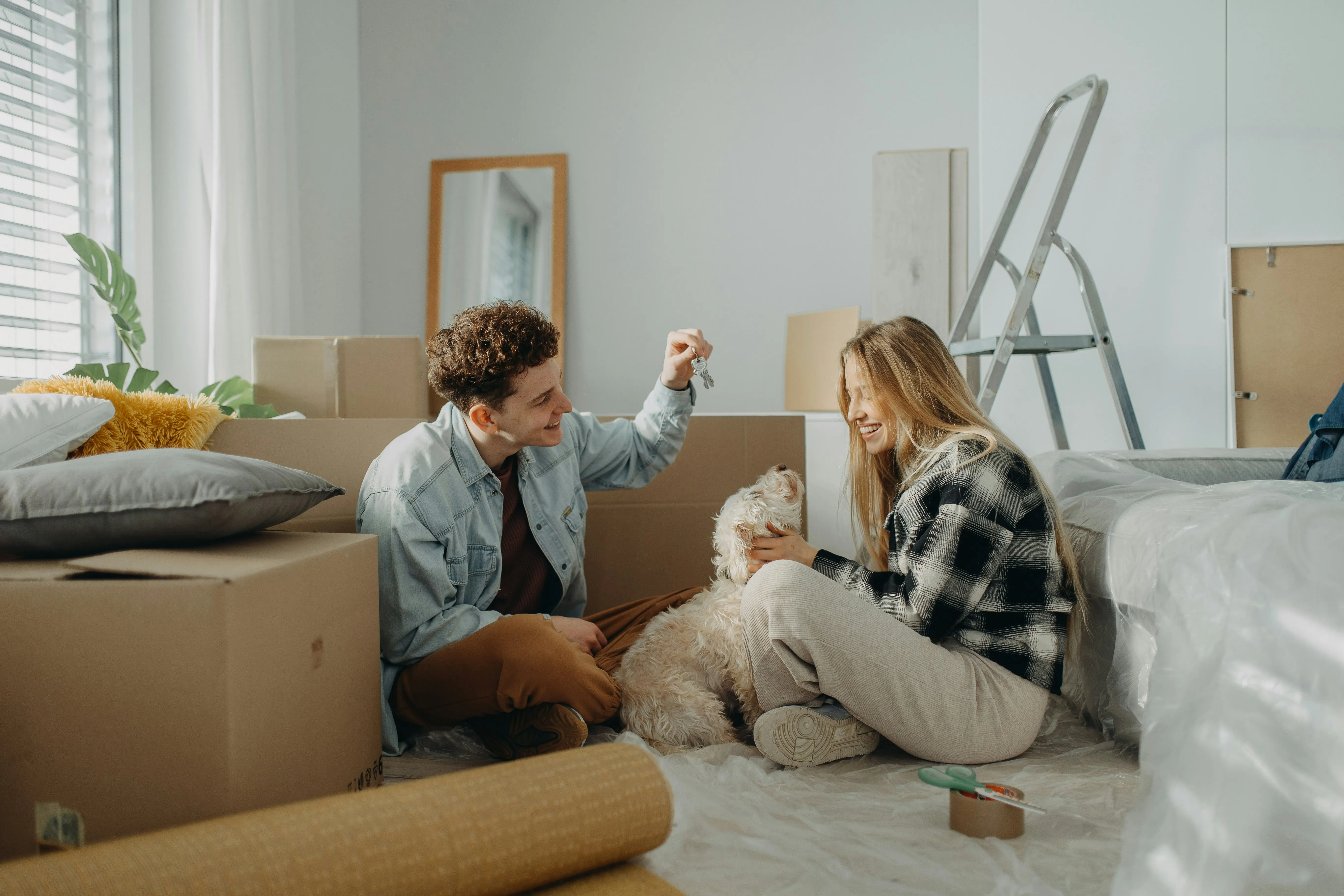 Happy couple with dog holding keys amongst moving boxes in new flat