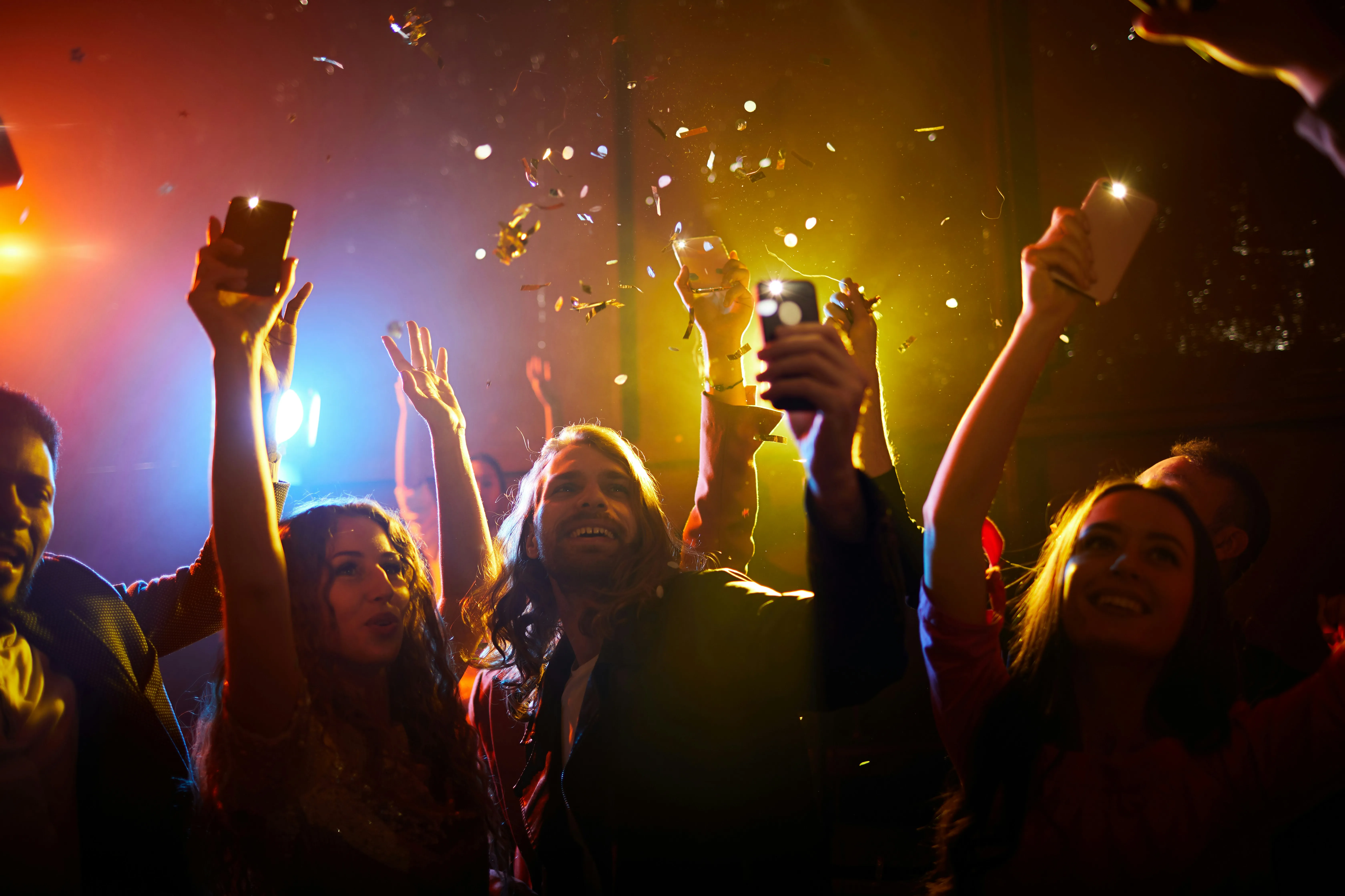 Partygoers enjoying a dynamic event with confetti, bright lights, and their phones in the air, creating an unforgettable atmosphere.