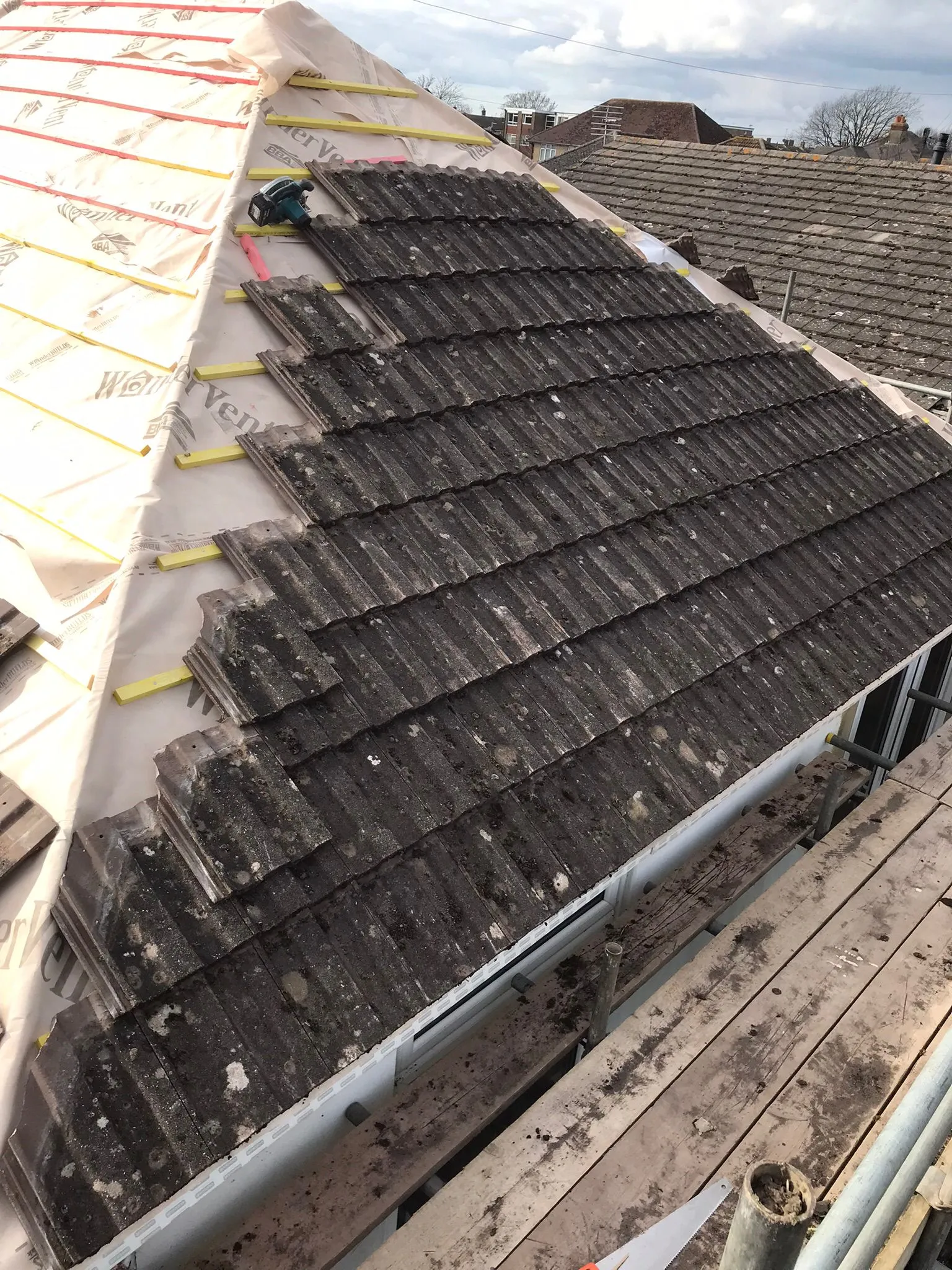 Pitched roof construction or repair showing old tiles, new underlayment, and timber battens.