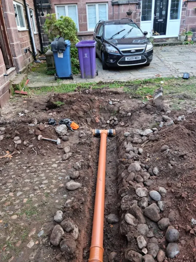 New orange drainage pipes being installed in a trench with soil and stones