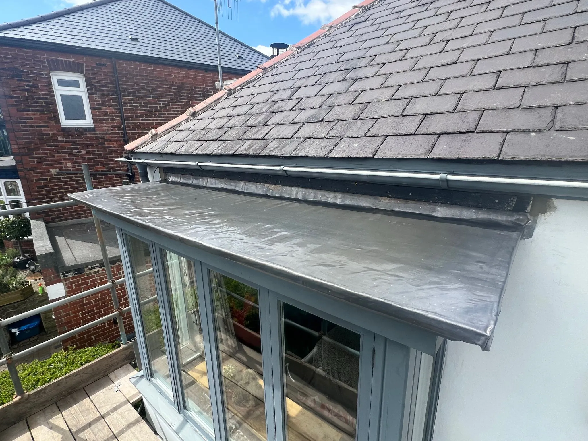 Pitched slate roof, flat roof section, new guttering, and scaffolding during roofing work
