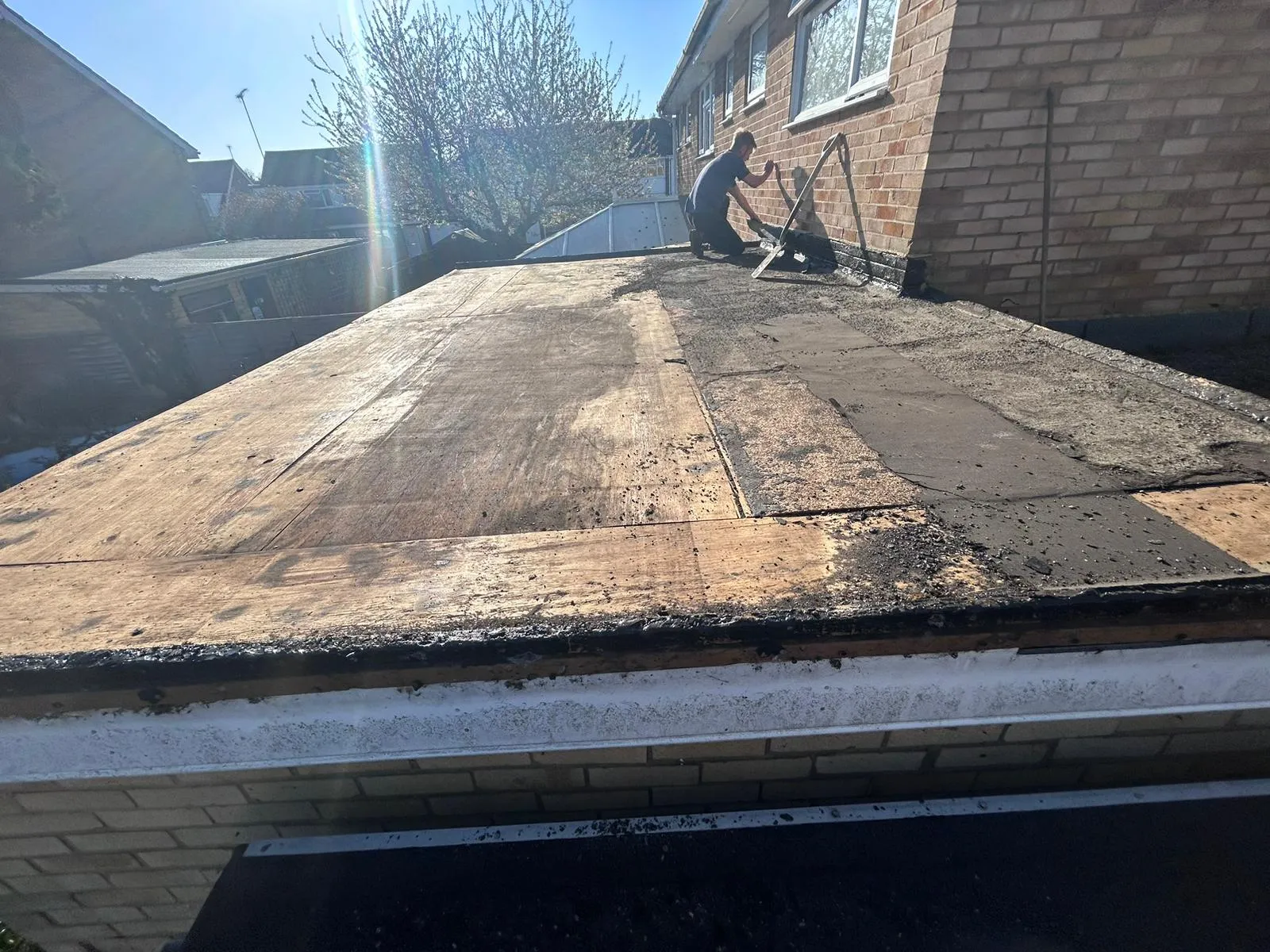 Roofer removing old felt from a flat roof deck during preparation.