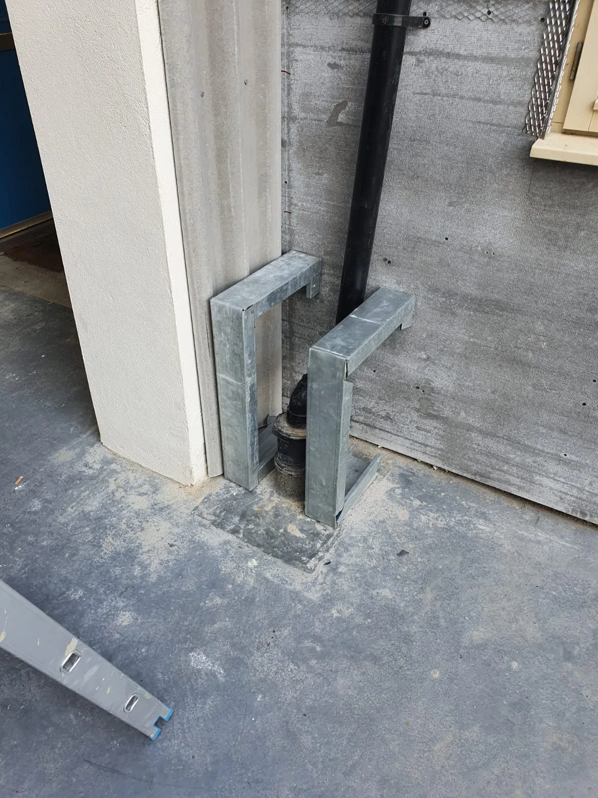 An exterior view of a building's downpipe emptying into a ground drain.