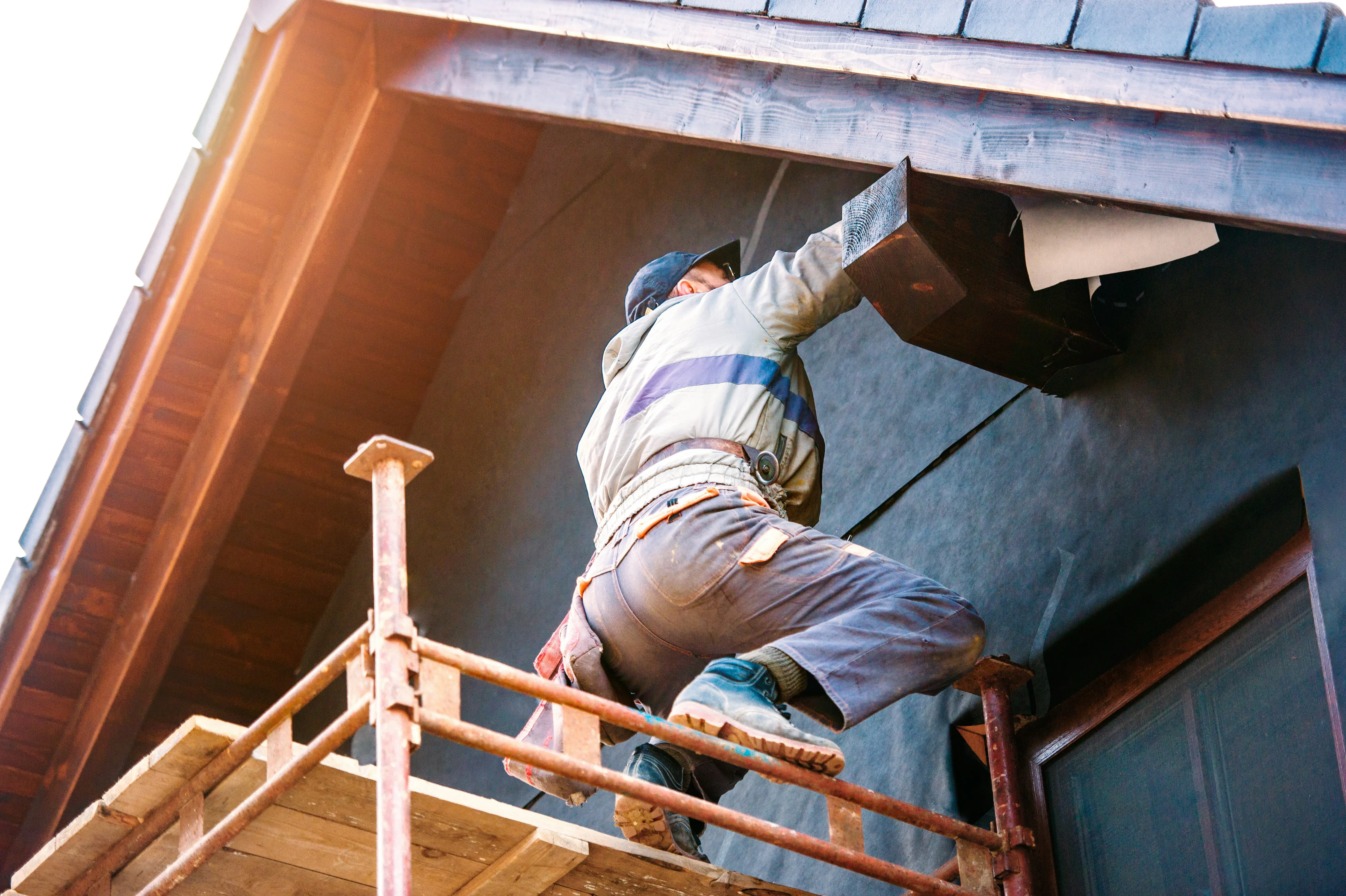 A professional roofer installing new uPVC fascia and soffit boards on scaffolding during a roofline upgrade.