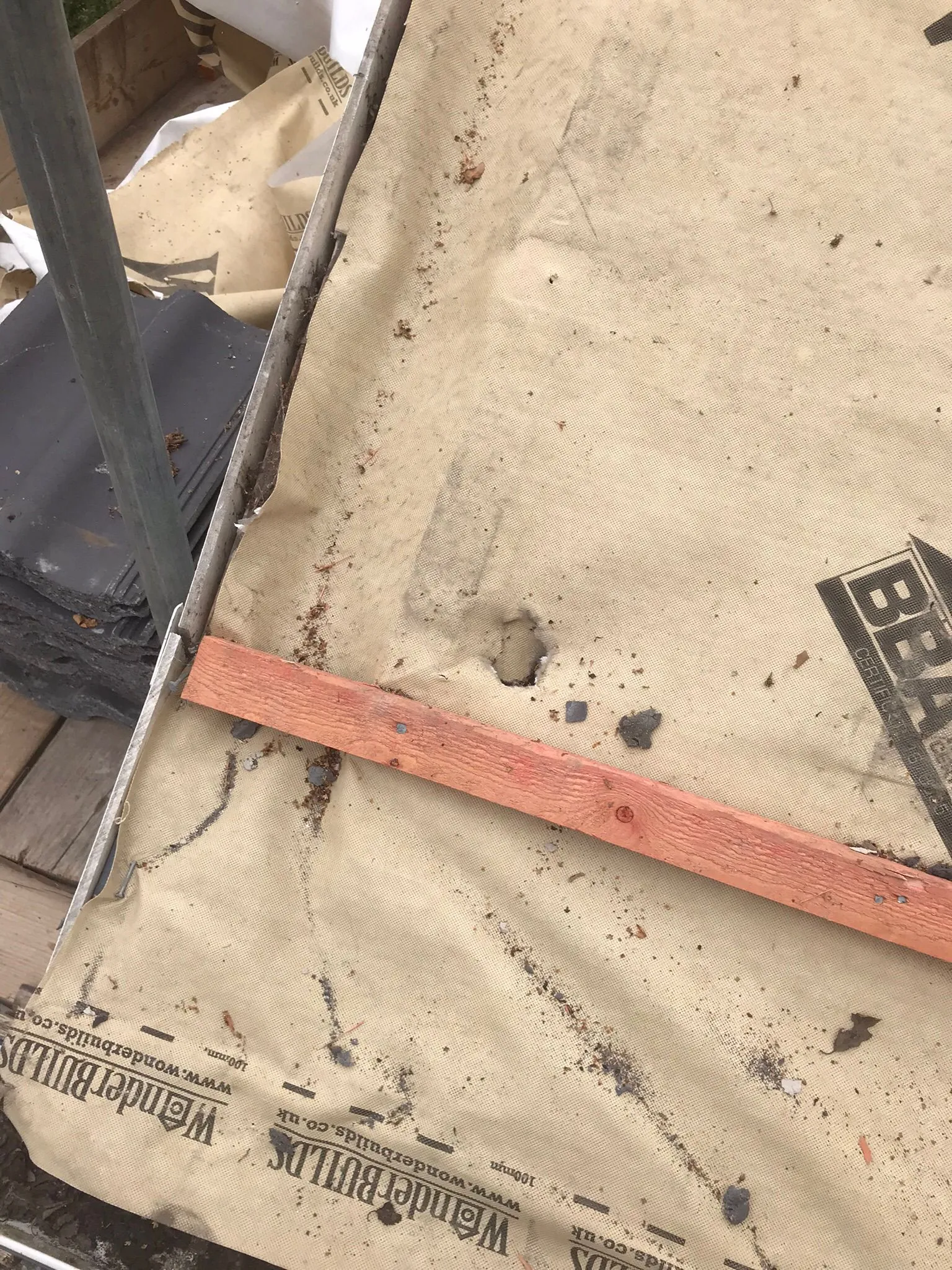 Roofing underlayment, slates, and a wooden batten on a roof during a construction or repair project.