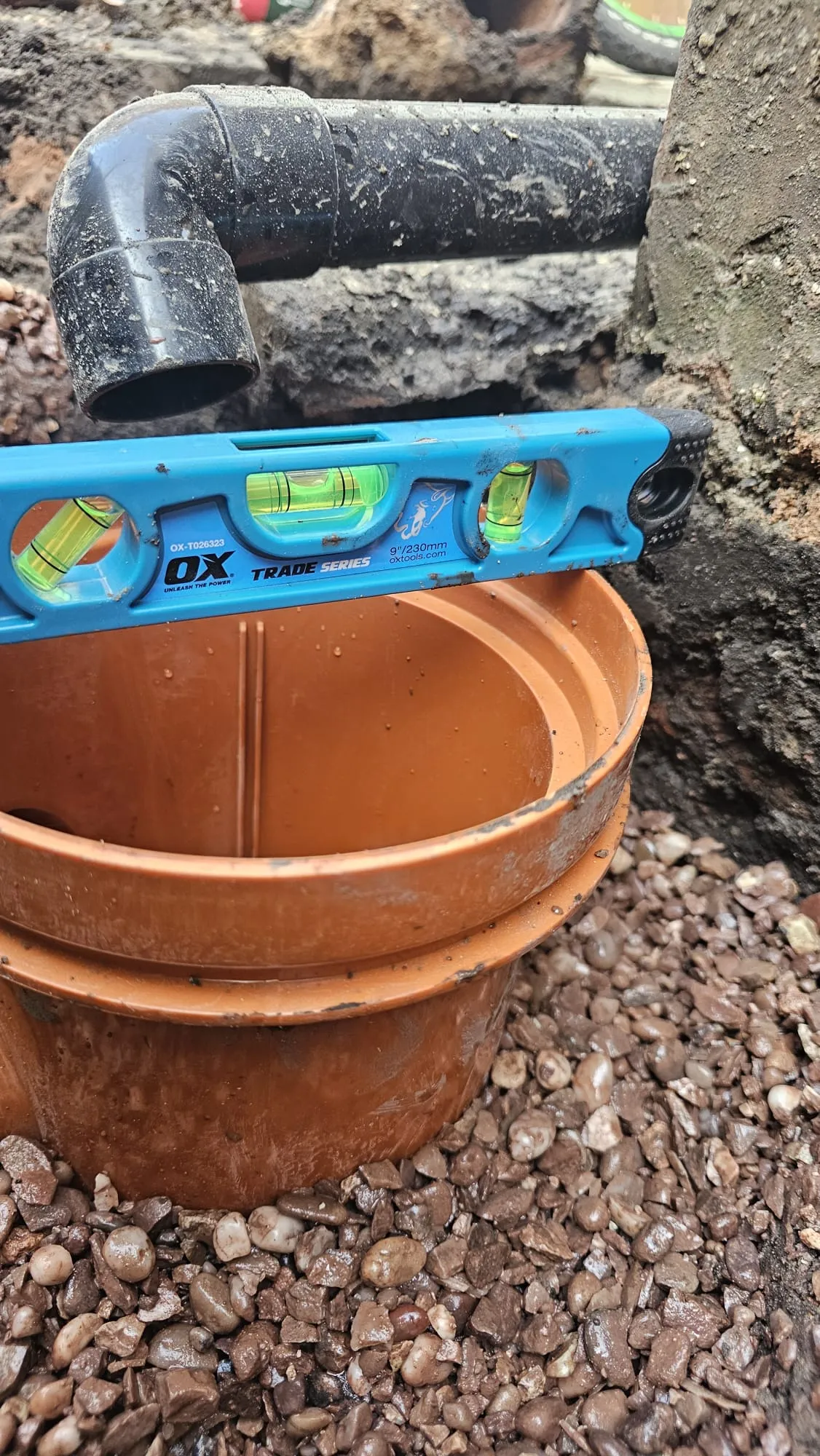 Drainage pipe and orange inspection chamber being installed and leveled during new drain construction or repair work.