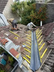 Two roofers repairing a pitched roof valley on a residential property.