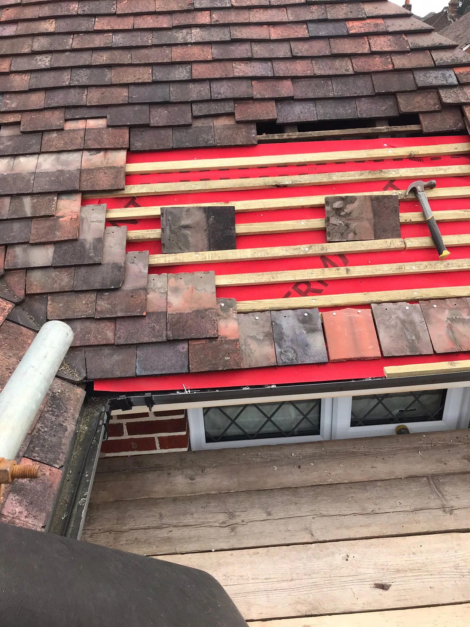 Roof repair in progress, with old tiles removed, exposing red underlayment and wooden battens for new tile installation.
