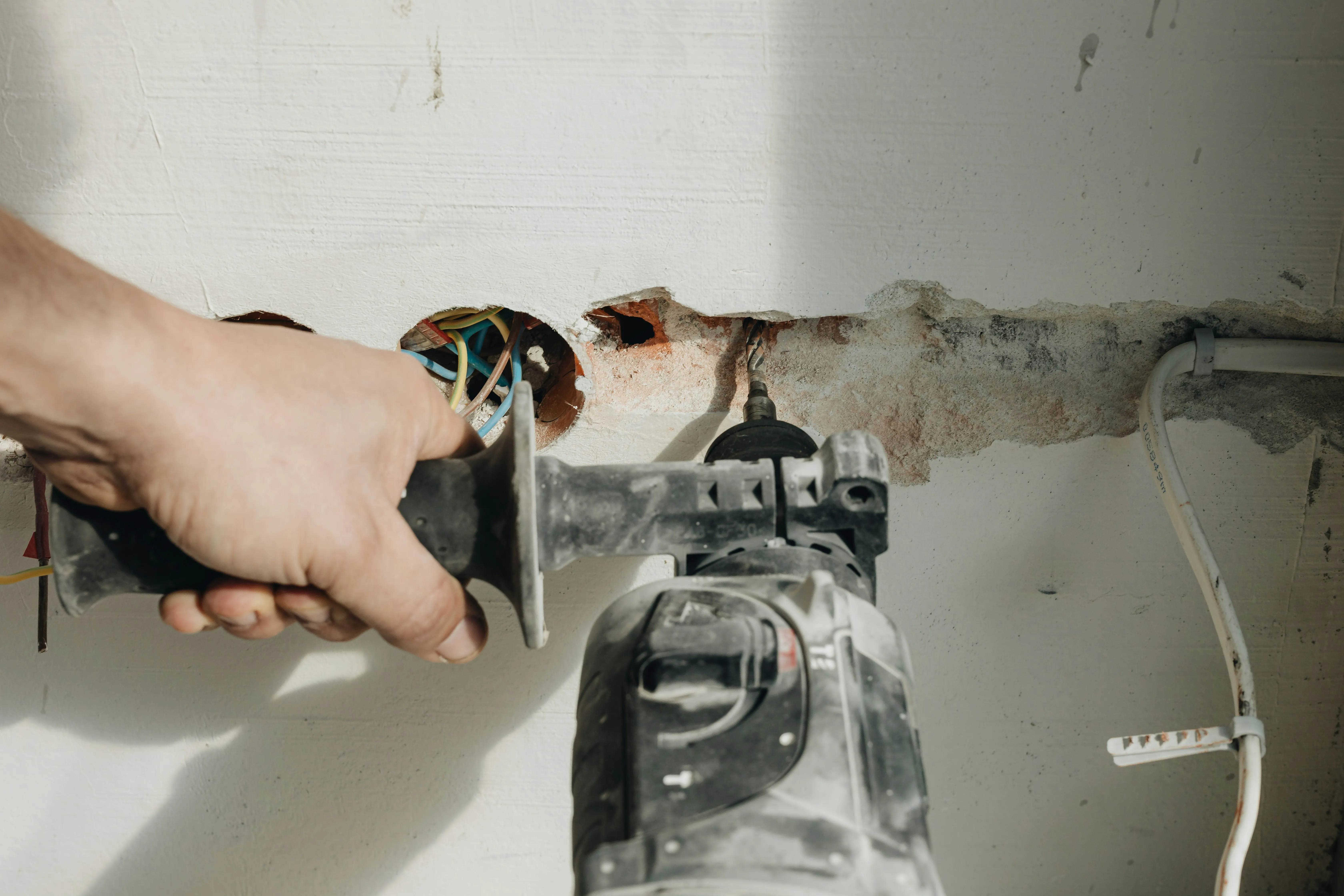 Electrician drilling into a wall during an electrical installation or rewire project.