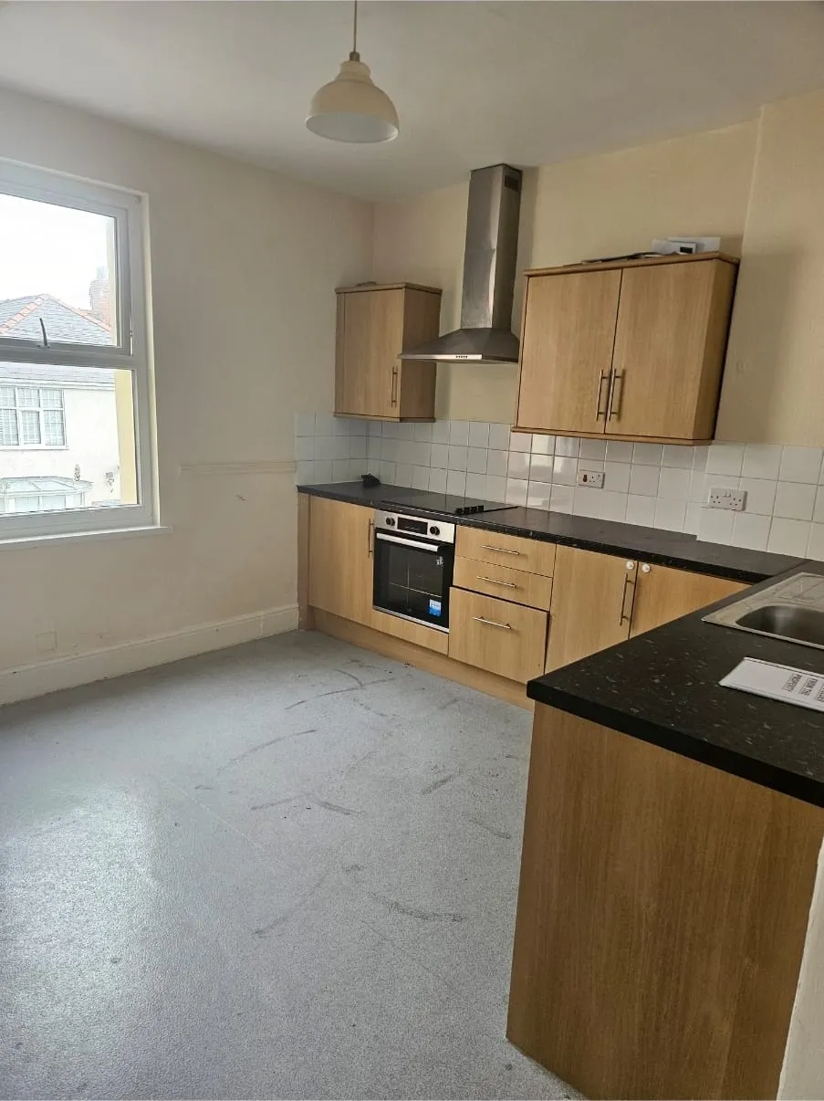 Empty kitchen with wooden cabinets, black countertops, and a window, reflecting a completed house clearance or end-of-tenancy service in North Wales.