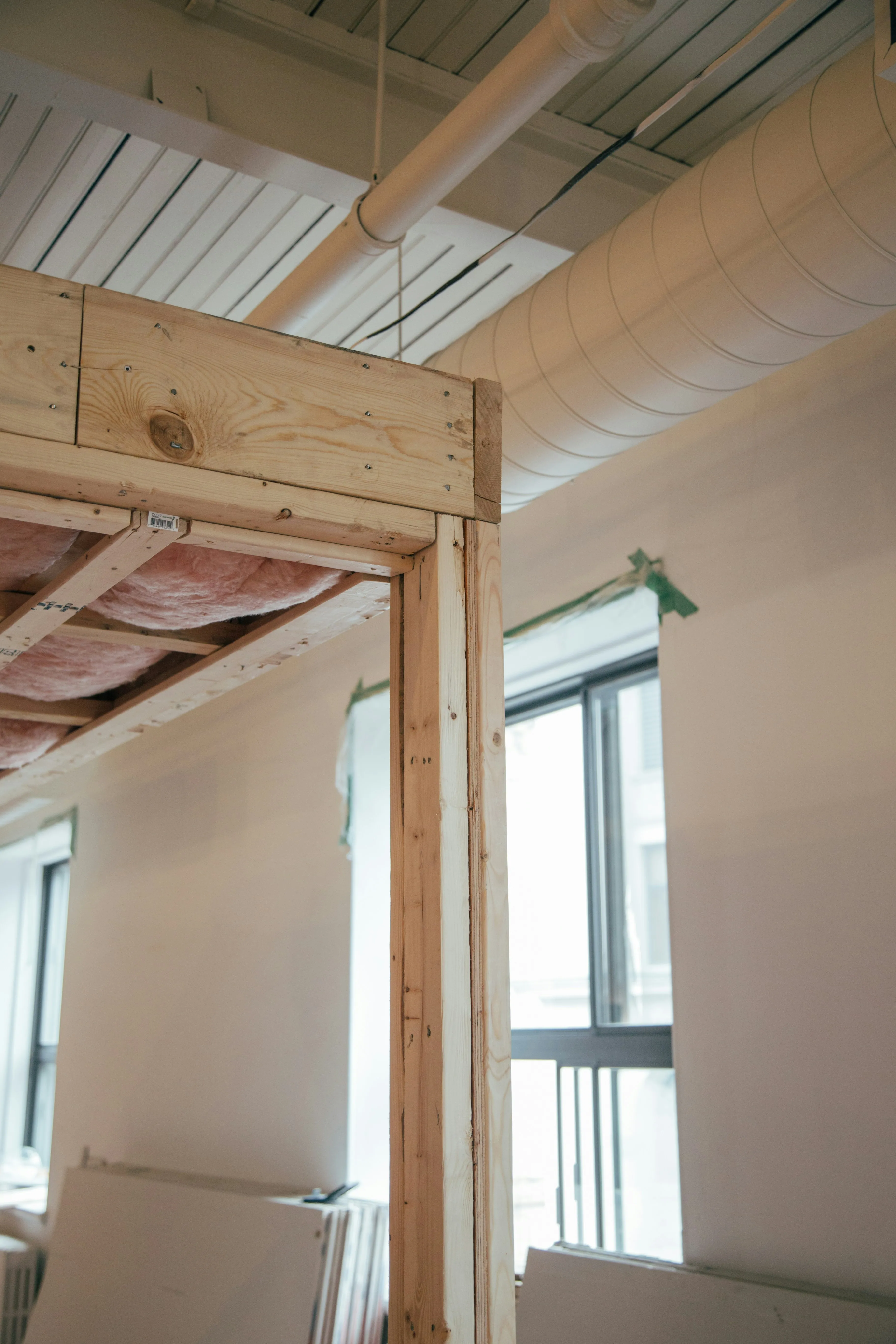 Interior view of wooden stud wall framing with pink insulation and plasterboard stacked nearby.