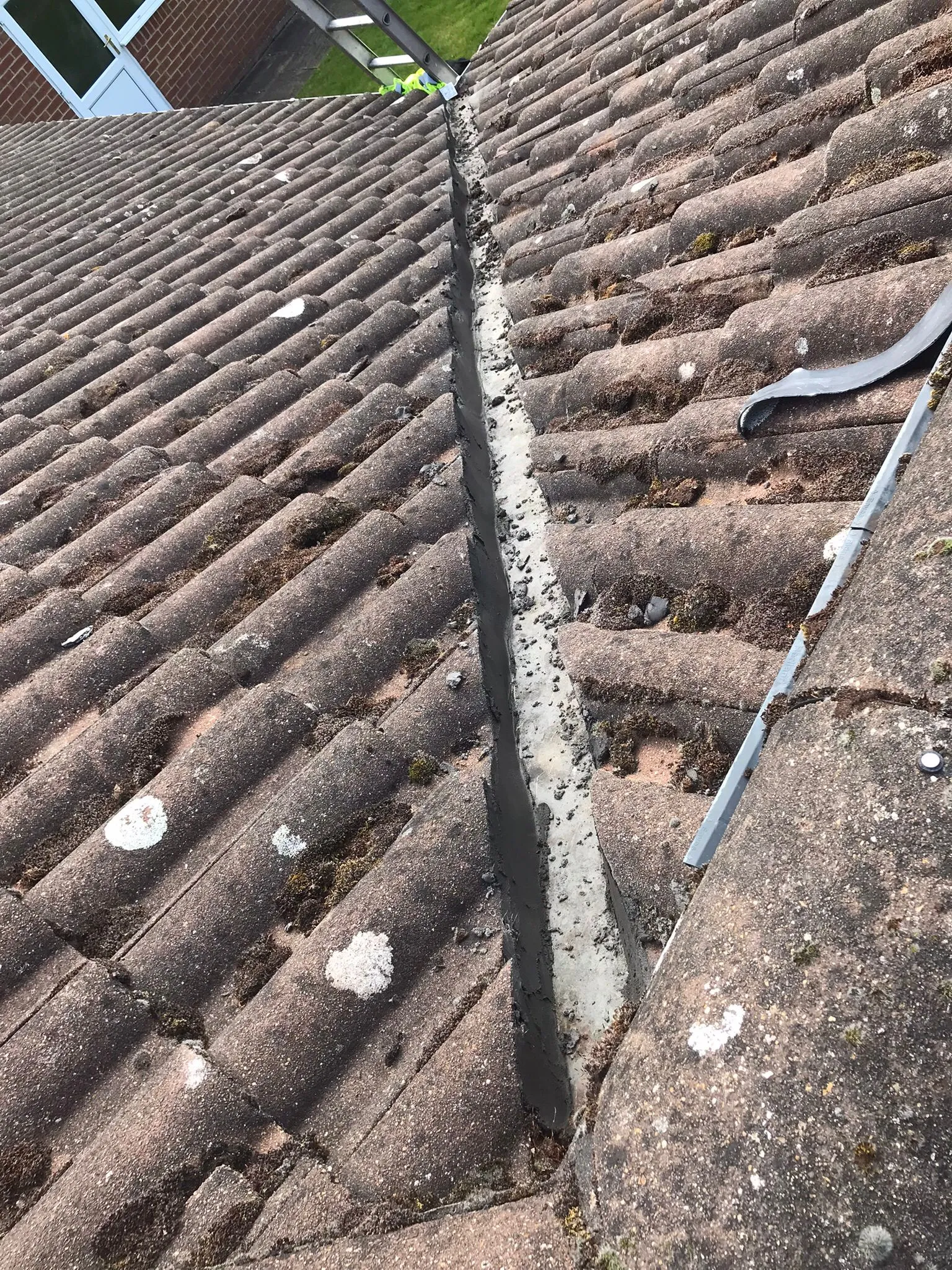 Close-up of a tiled roof with moss and a valley that appears to be filled with debris or mortar, indicating a need for repair or maintenance.
