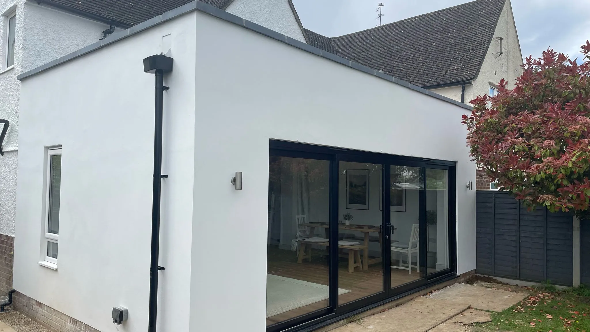 Modern white home extension in Cheltenham with black sliding doors and flat roof.