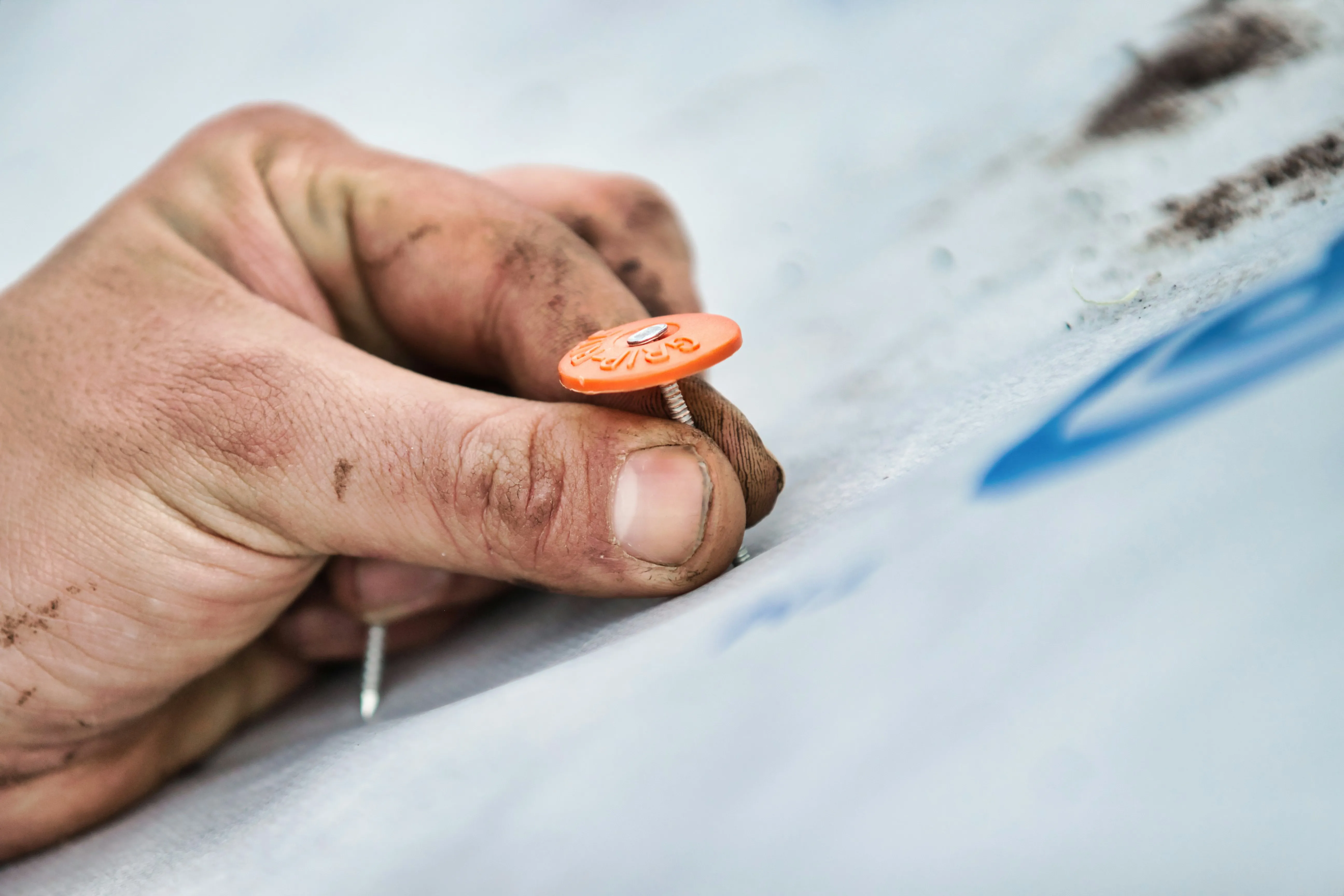 A roofer's hand securing breathable roofing membrane with a cap nail on a new roof installation.