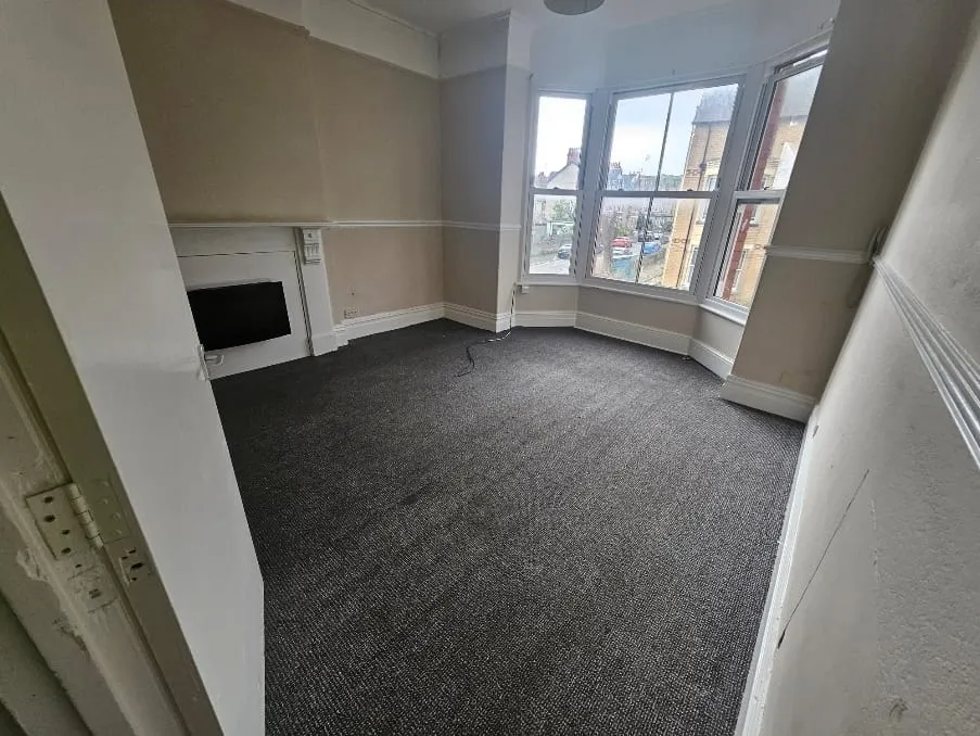 Empty room with grey carpet, bay window, and fireplace after professional house clearance in Llandudno