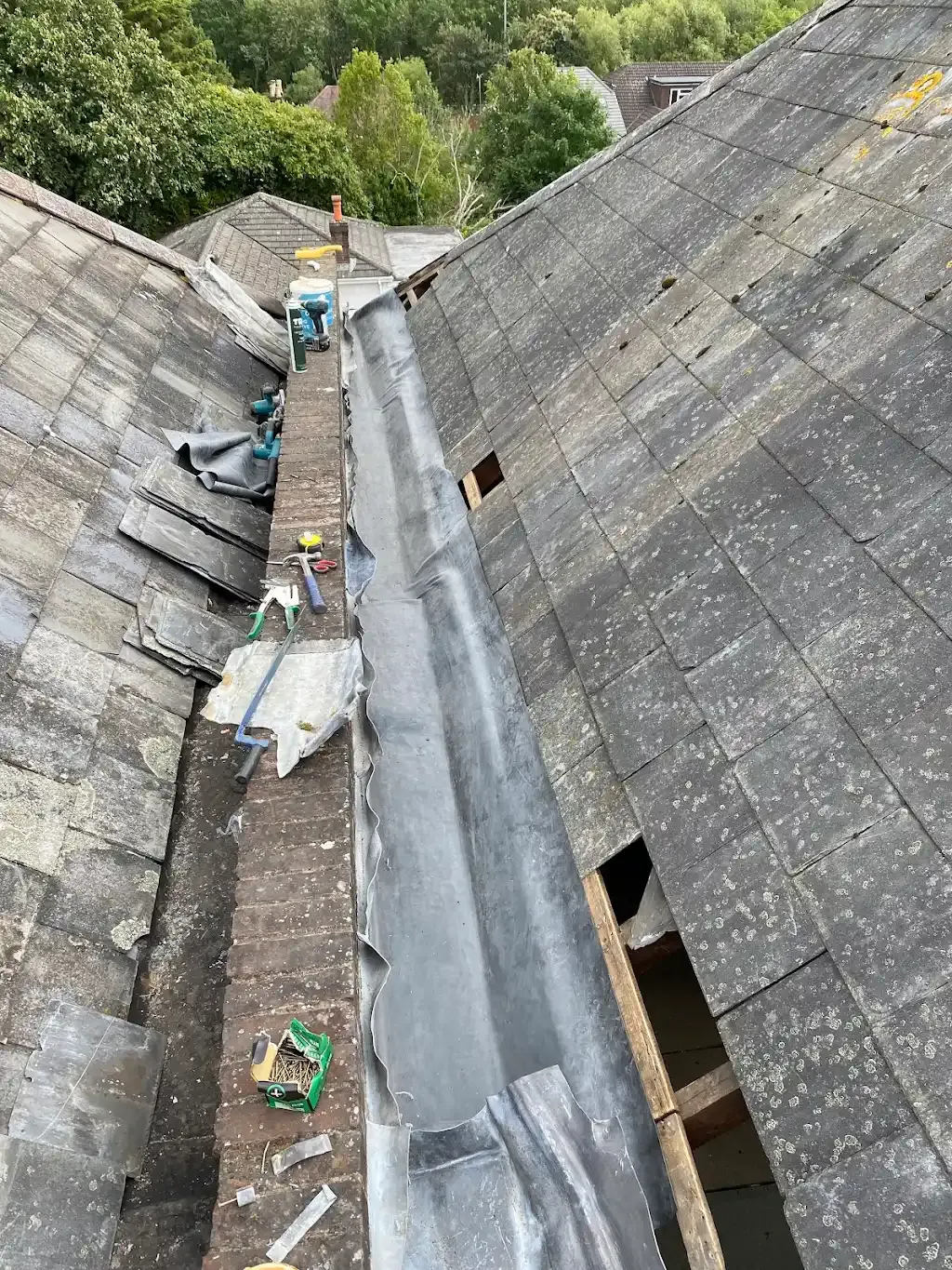Roof valley repair in progress with new lead flashing, tiles, and tools visible