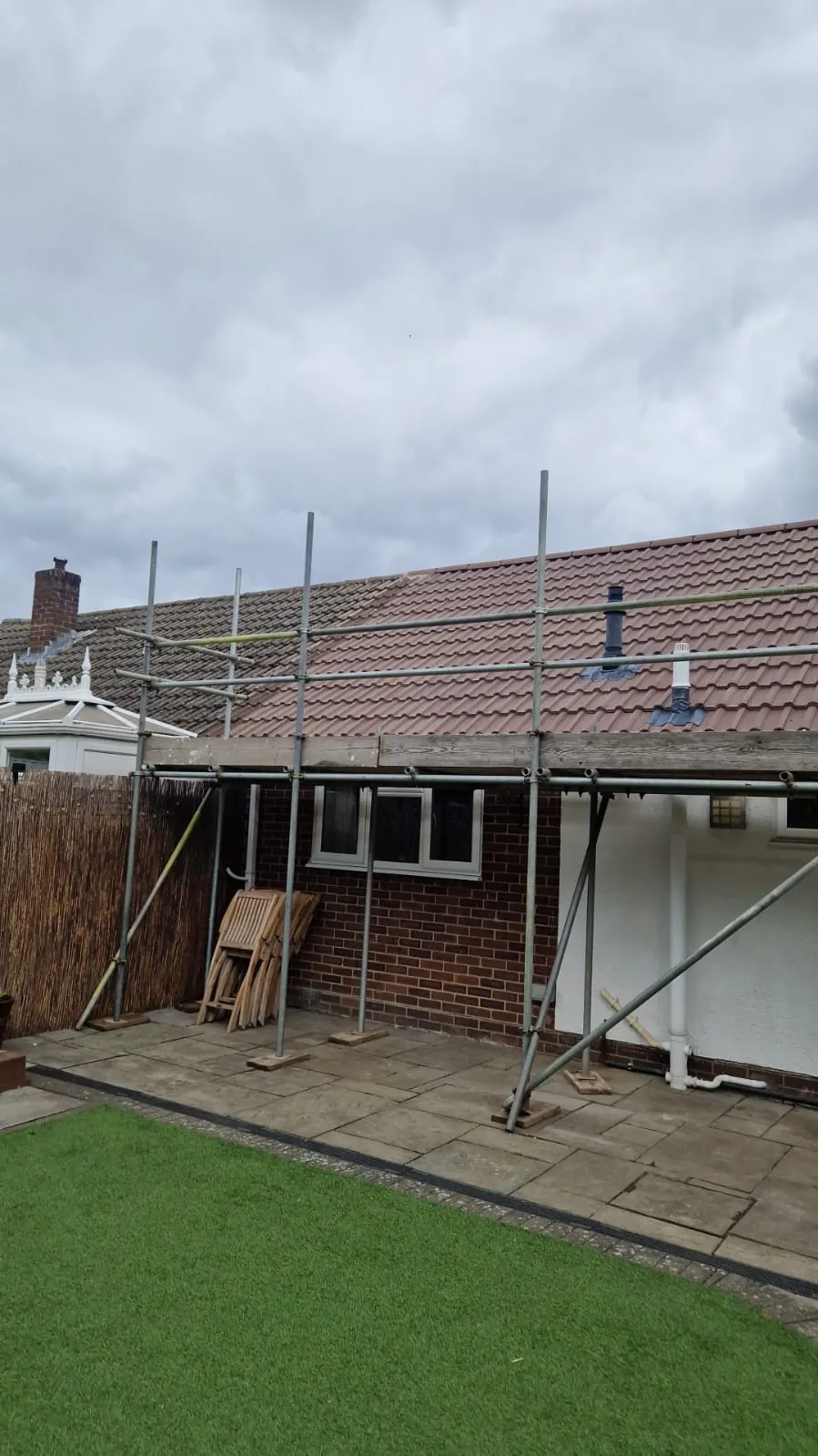Scaffolding set up next to a house with a red tiled roof, indicating preparation for roofing services.