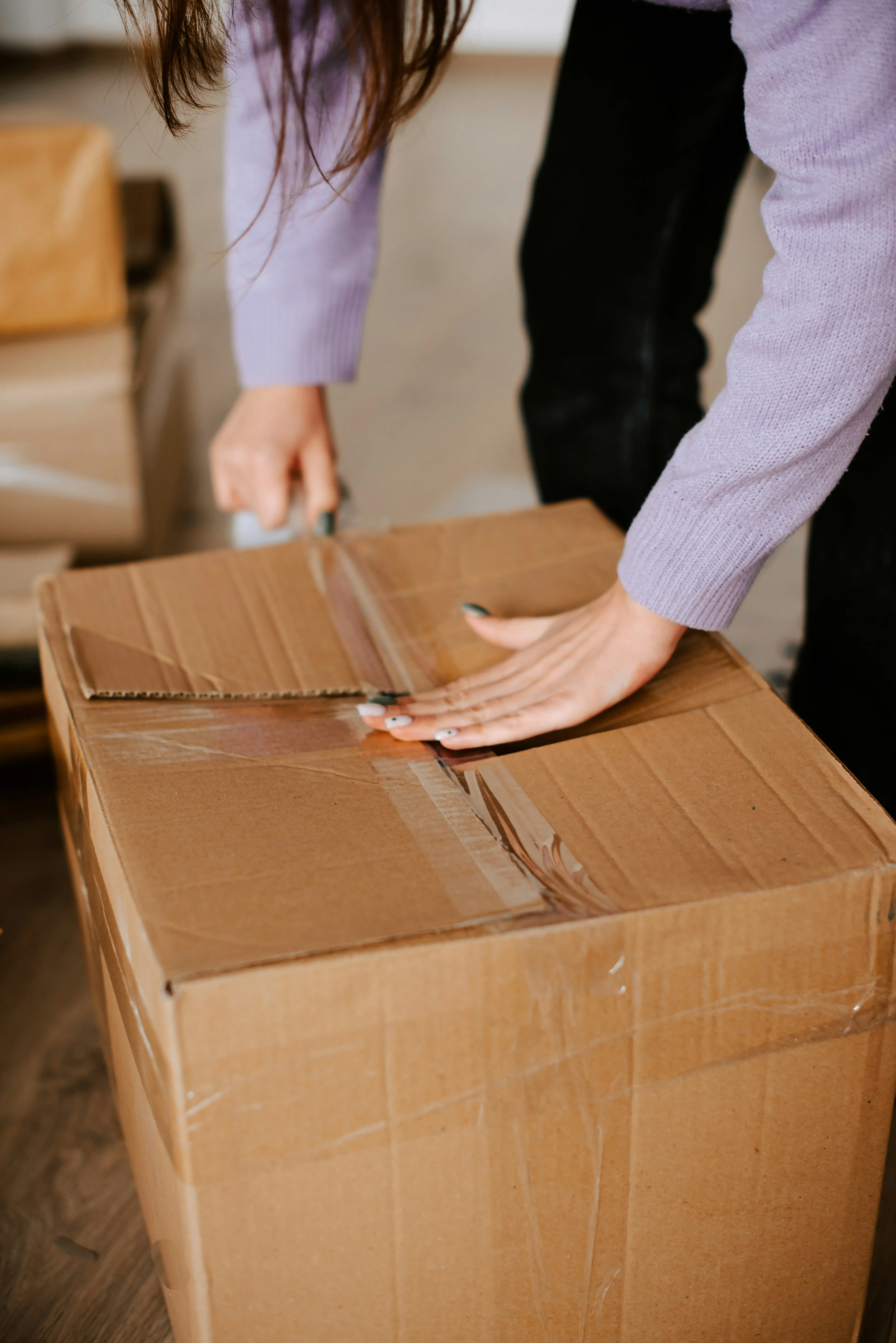 Close up of hands taping a cardboard box with packing tape, showing the packing process for a move.