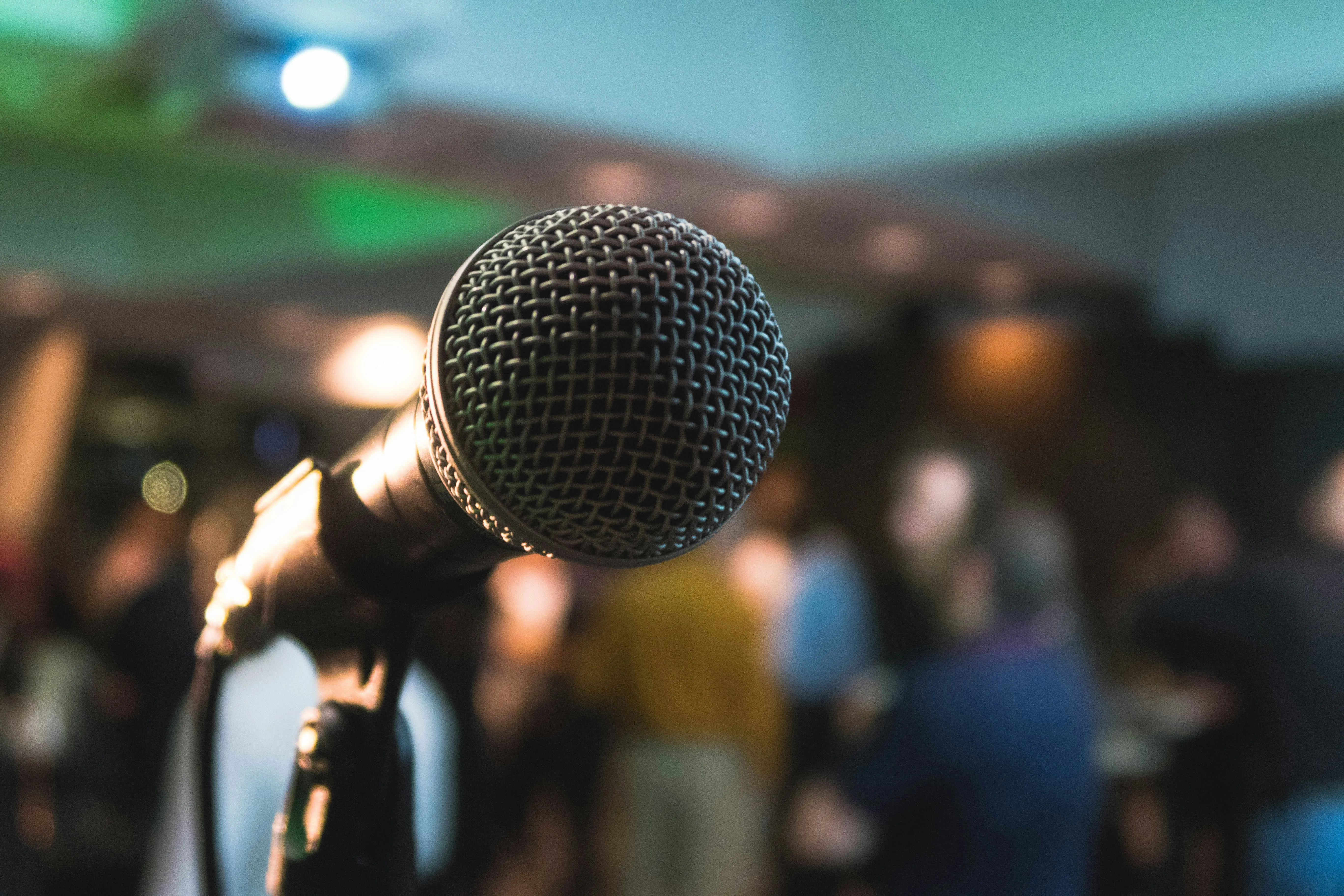 Close-up of a professional stage microphone at a party or event, with soft focus lights and people in the background.
