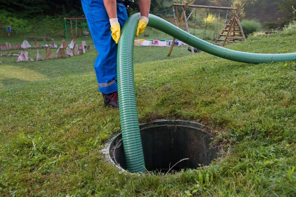 Drainage engineer using a large hose for drain cleaning or maintenance of an outdoor manhole.