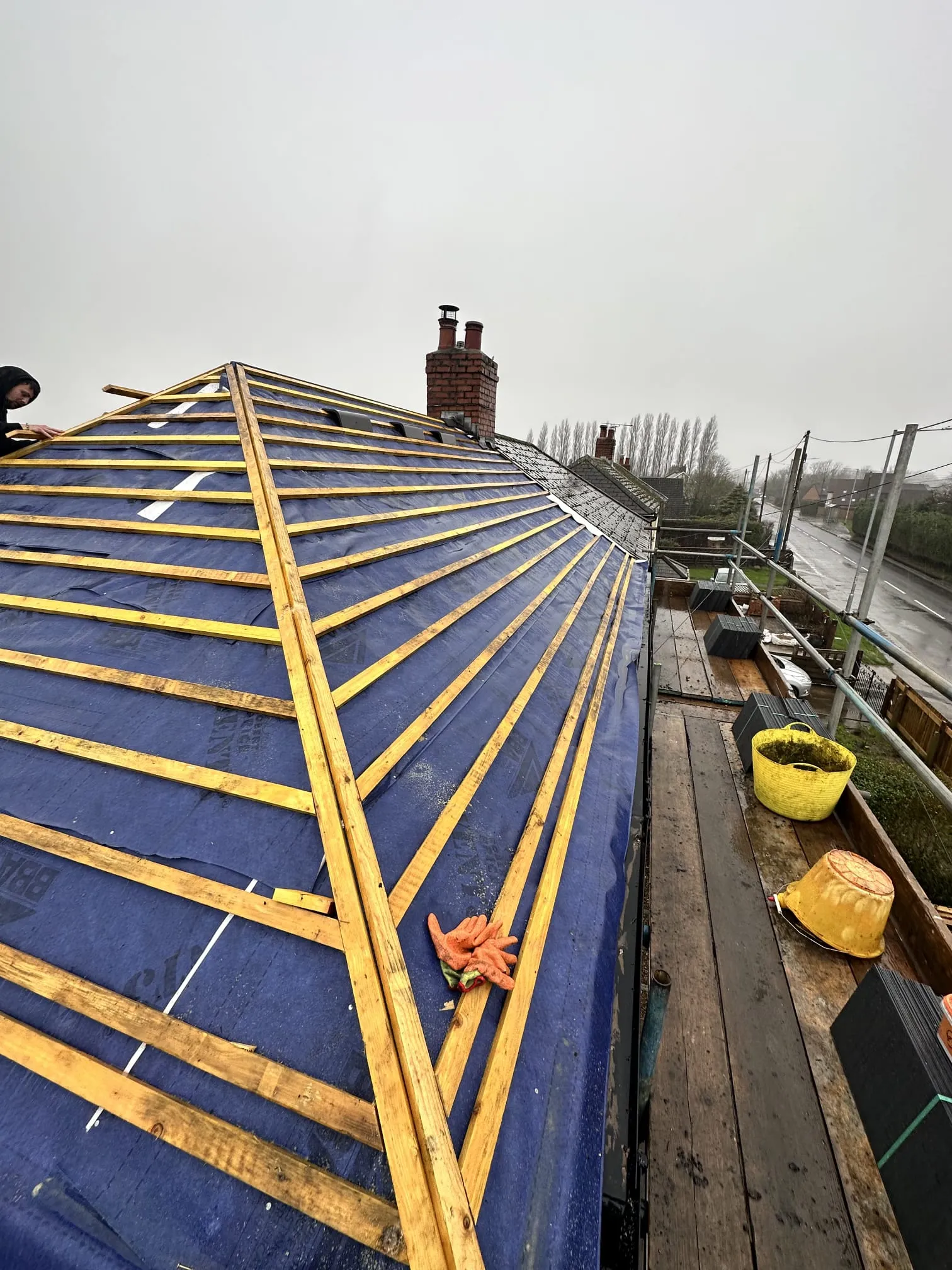A roofer on a roof with blue waterproof membrane and new wooden battens, indicating a re-roofing project.