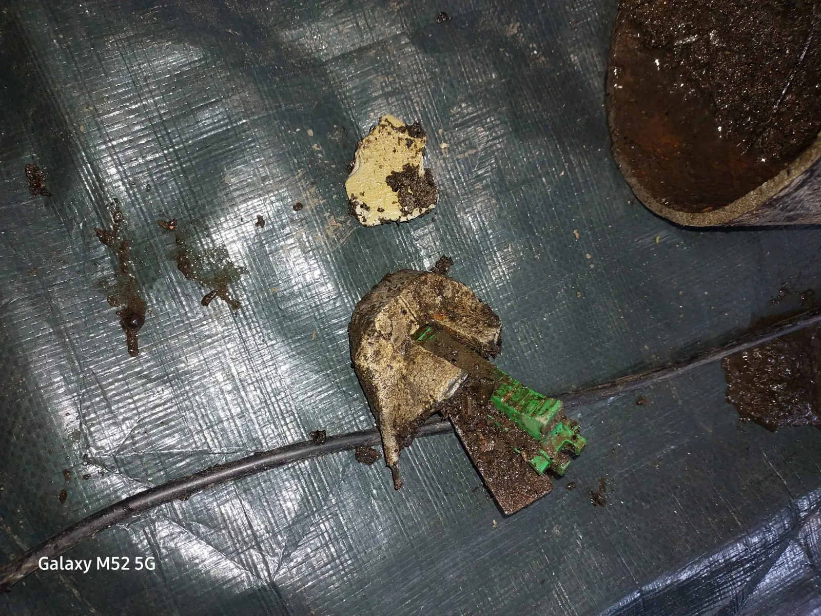 Various muddy debris and a broken pipe section on a green tarp, likely removed from a drain during unblocking or repair.
