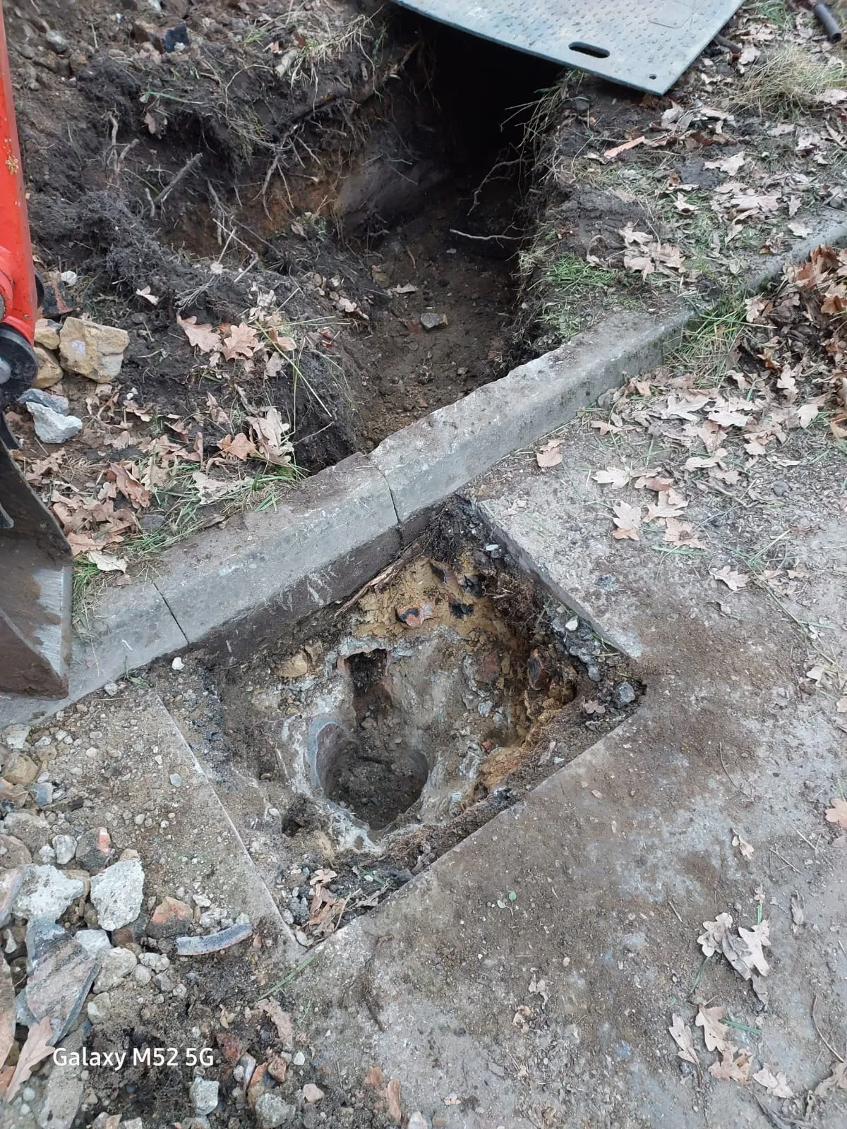 An open manhole or drain inspection chamber in an excavated area on the ground, suggesting drainage repair or new installation.