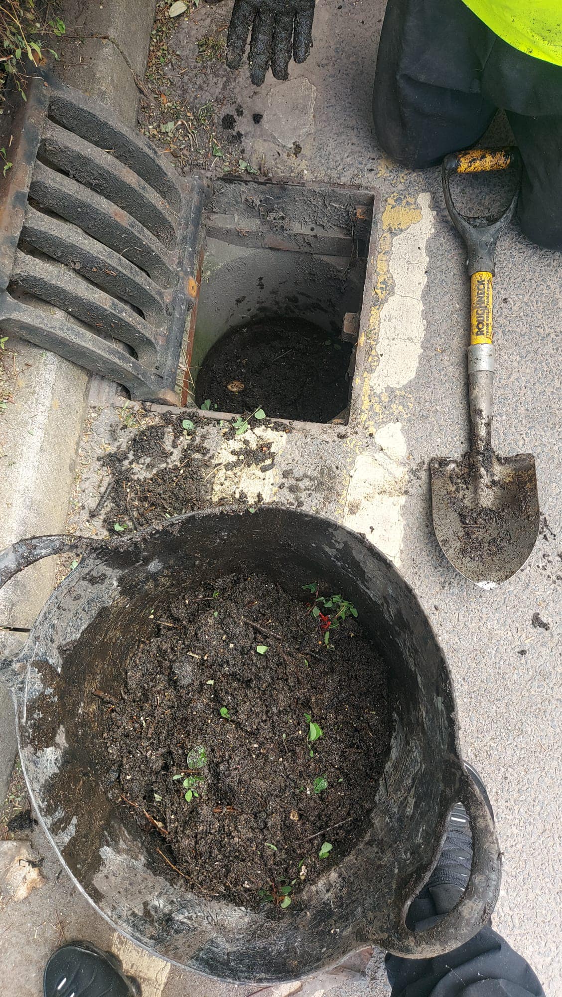 Local drainage engineer clearing a blocked stormwater gully in Exeter with a shovel and bucket