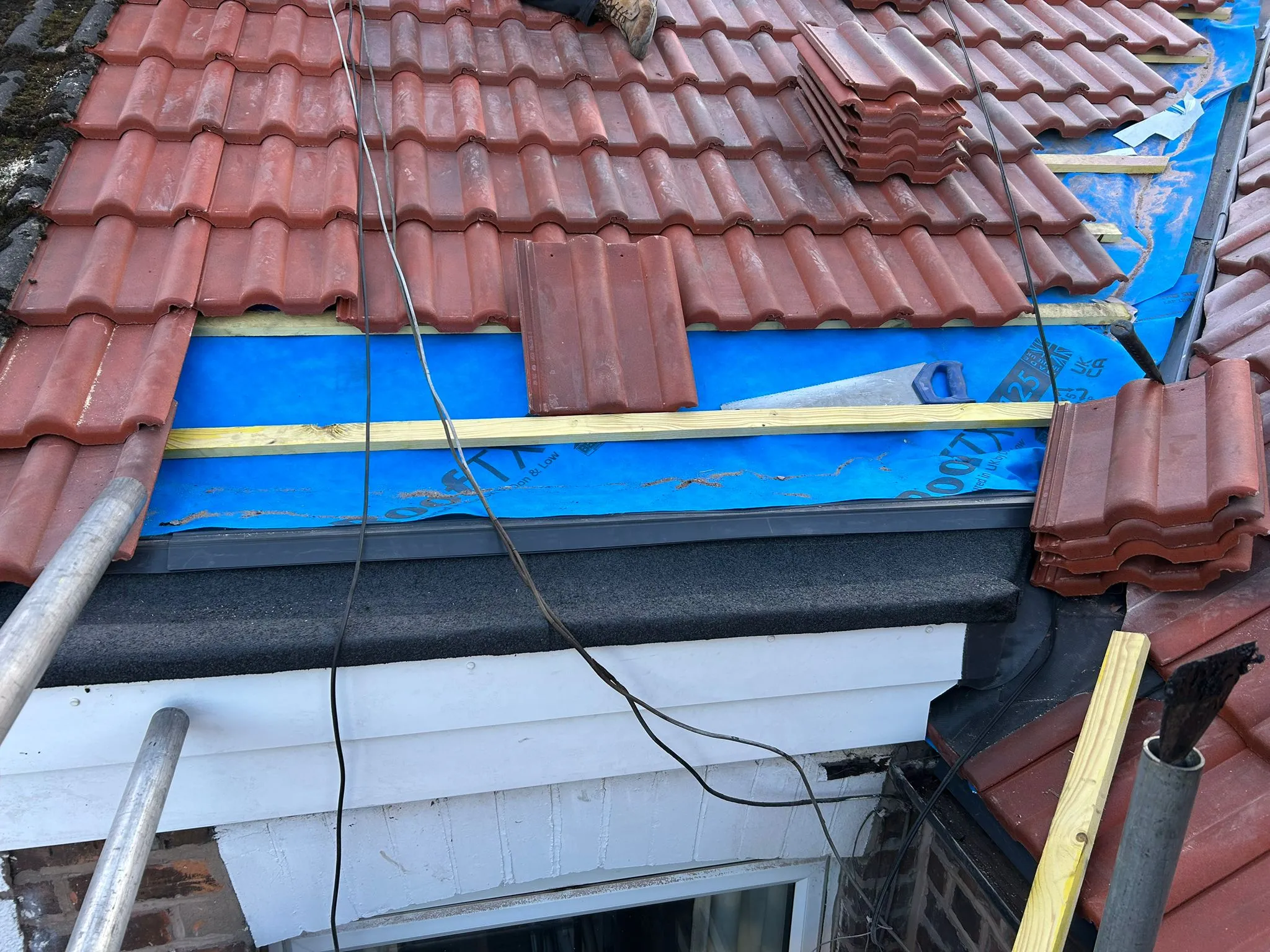Pitched roof construction in progress with red tiles, blue underlayment, and wooden battens