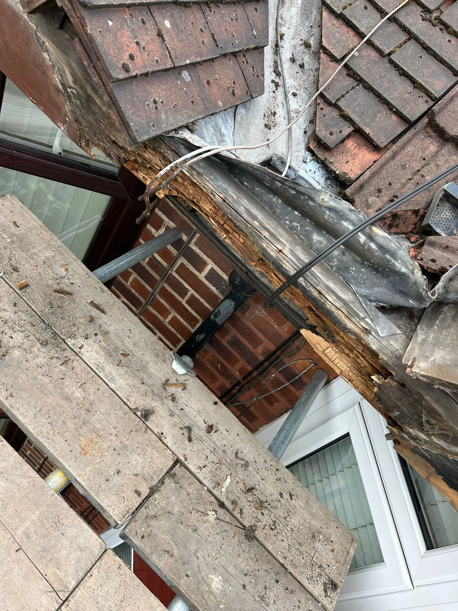 Severe timber rot and damage on a roof, showing degraded wood, tiles, and lead flashing, with scaffolding in the foreground.
