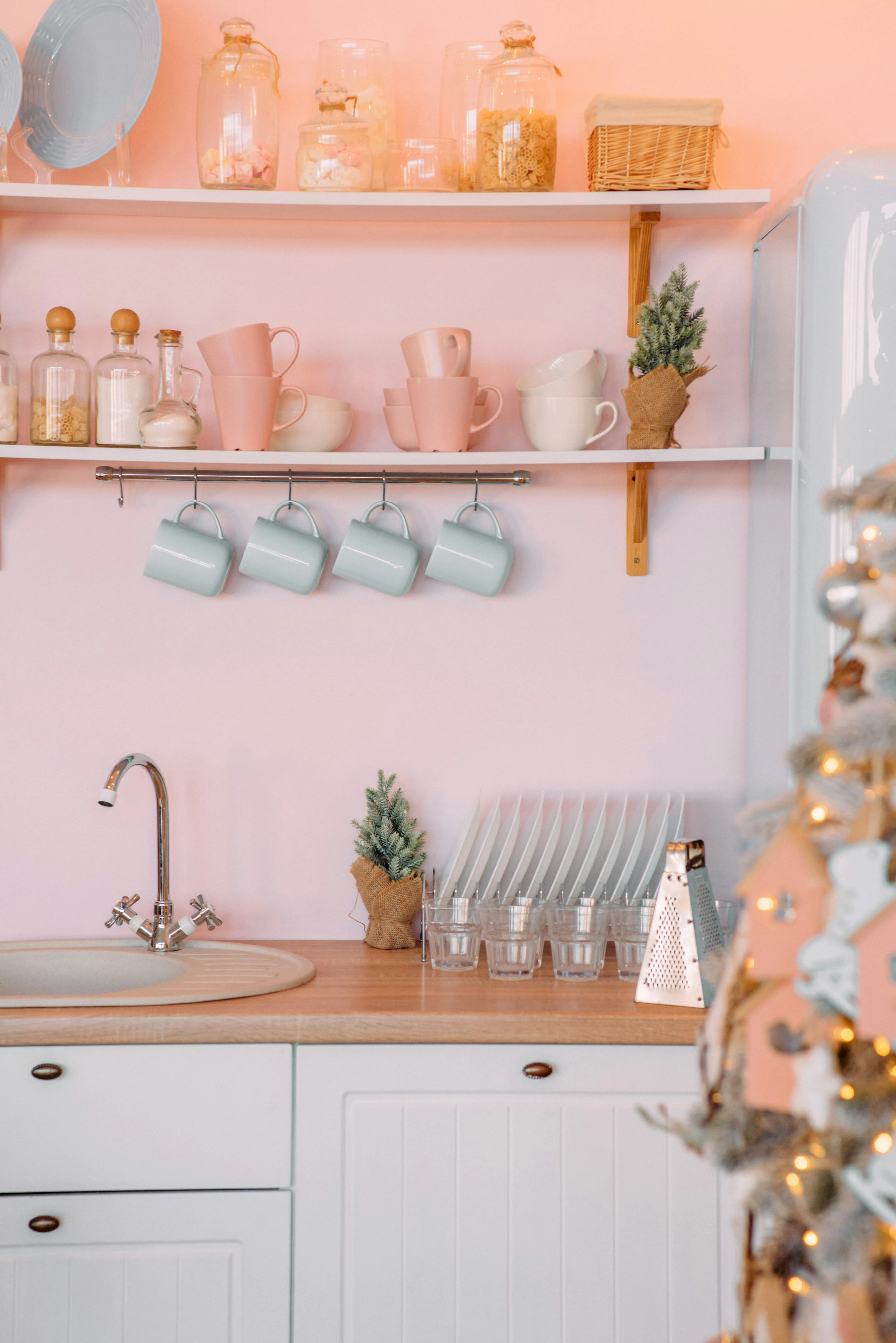 A colourful and tidy kitchen interior with pink walls and white cabinets.