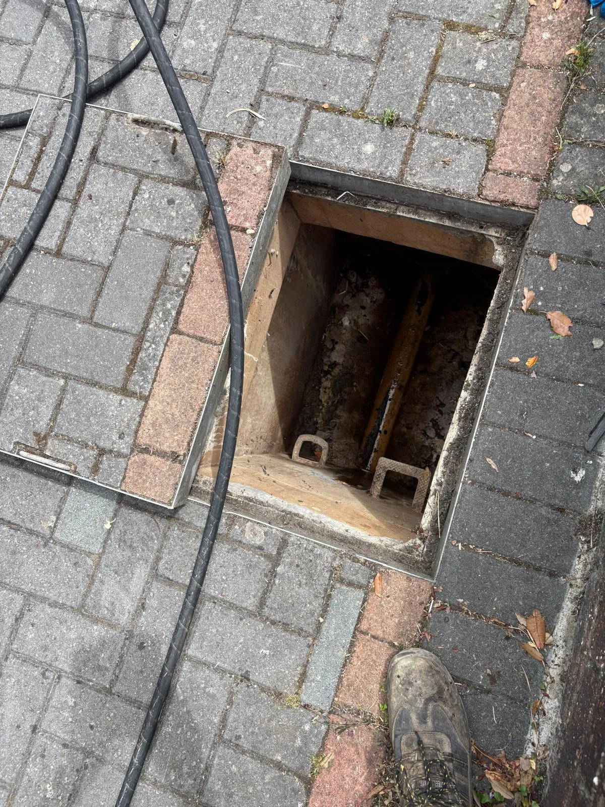 Drainage technician using a high-pressure water jetting hose in an open manhole to clear a blockage or clean the drain.