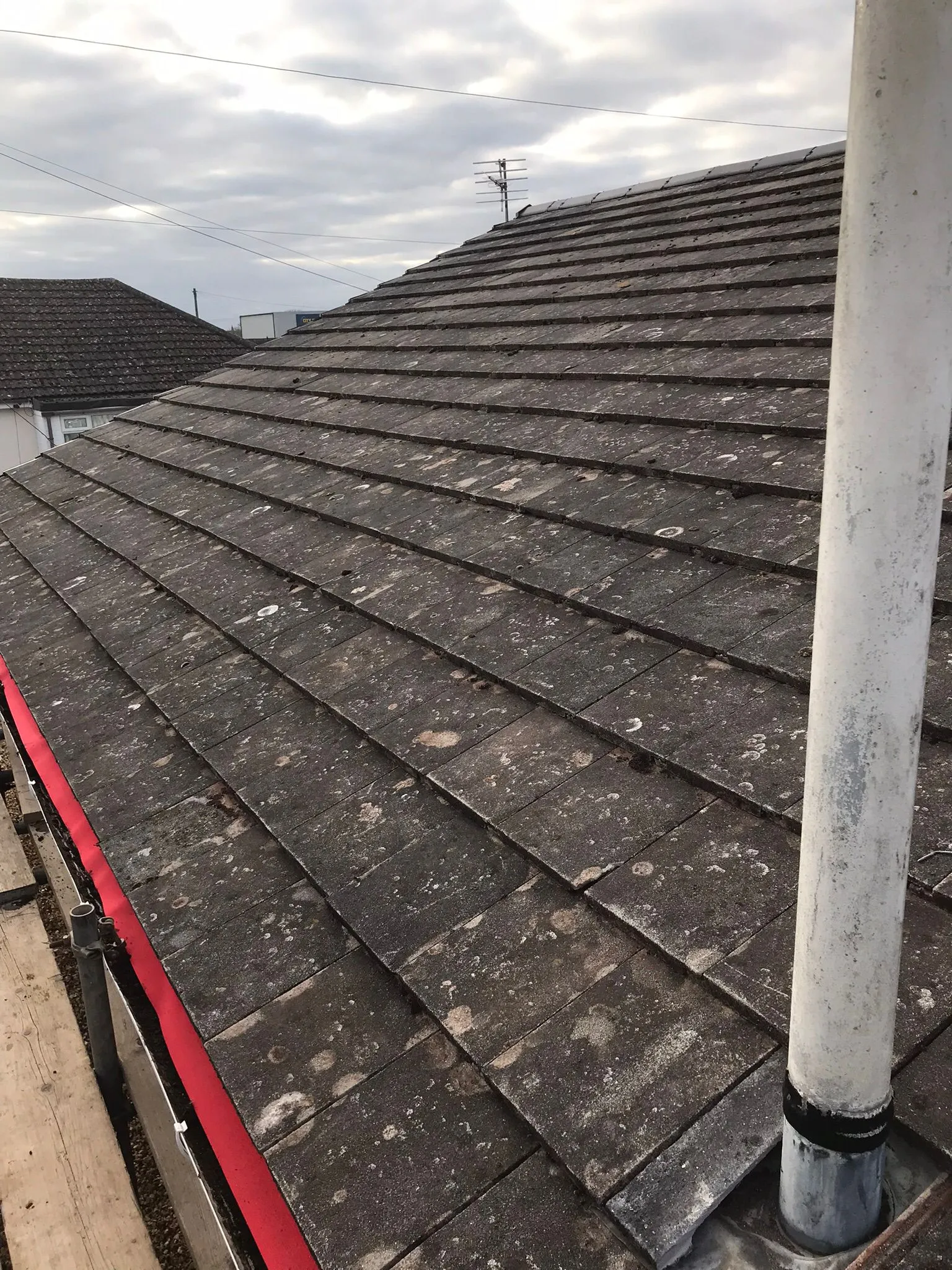Weathered tiled roof with lichen, a vent pipe, and scaffolding, indicating repair or maintenance work.