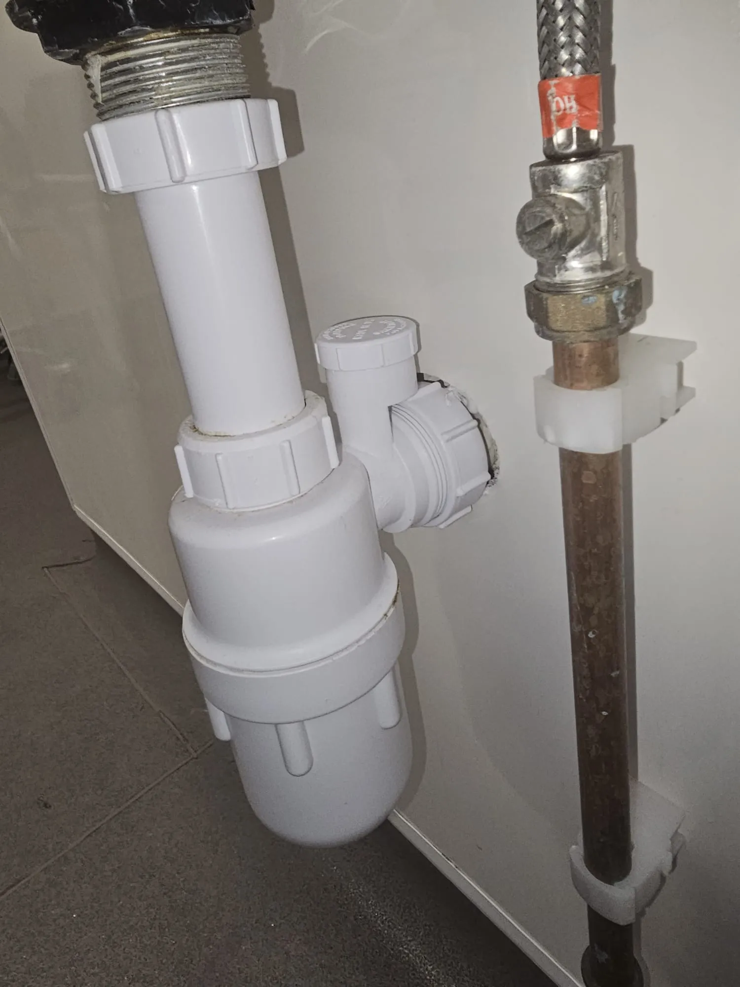 A white bottle trap and copper plumbing under a sink, demonstrating Ecodrain Solutions' drainage installation services.