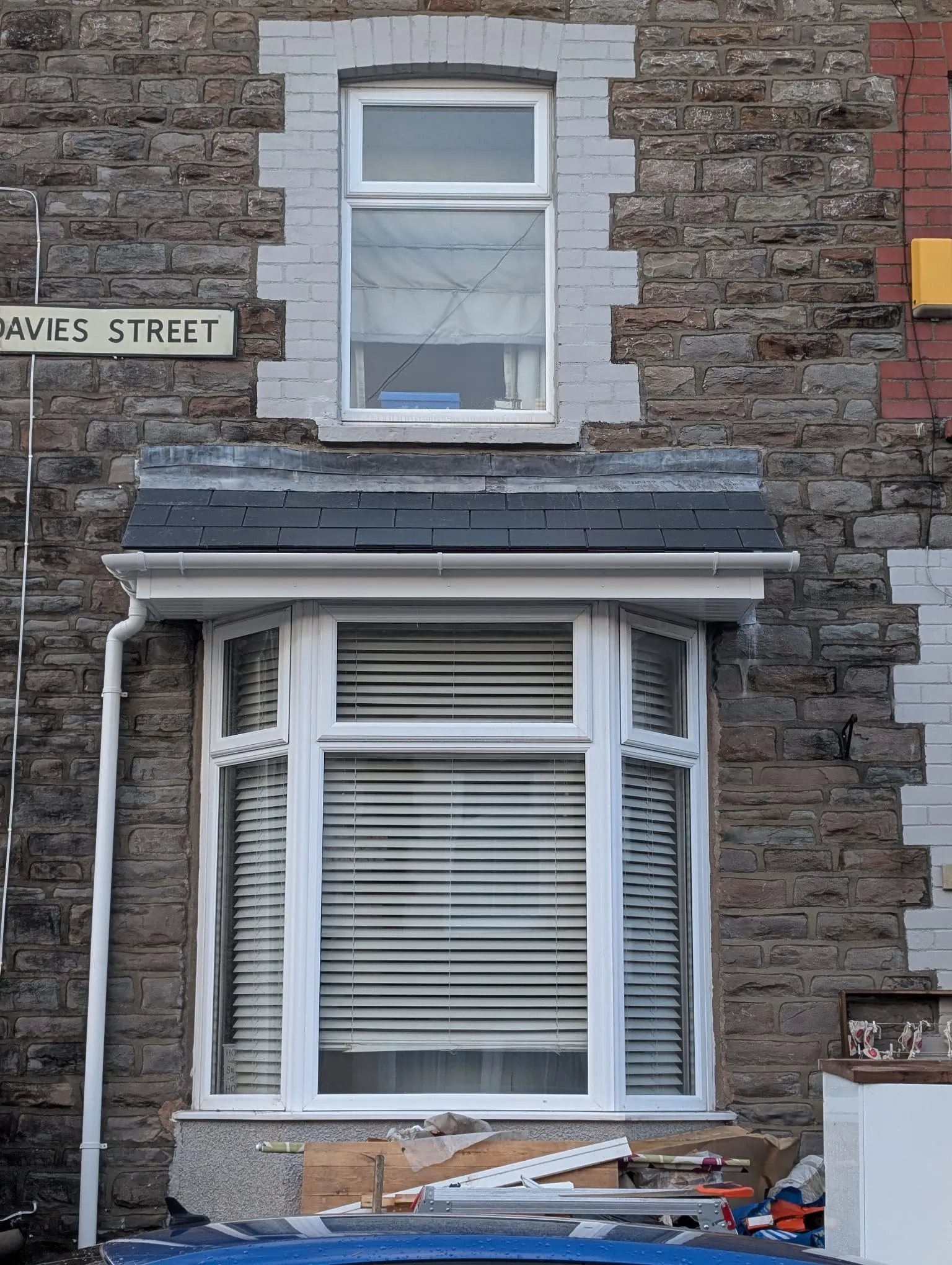 A house exterior featuring new white uPVC guttering, a downpipe, and a dark grey tiled canopy above a bay window.