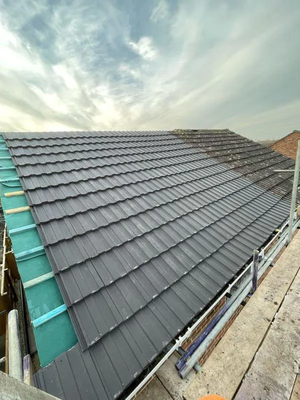 Installing new dark grey concrete tiles on a pitched roof with green underlay and scaffolding.