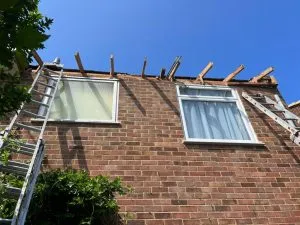 House under construction with exposed wooden rafters for a new pitched roof installation.
