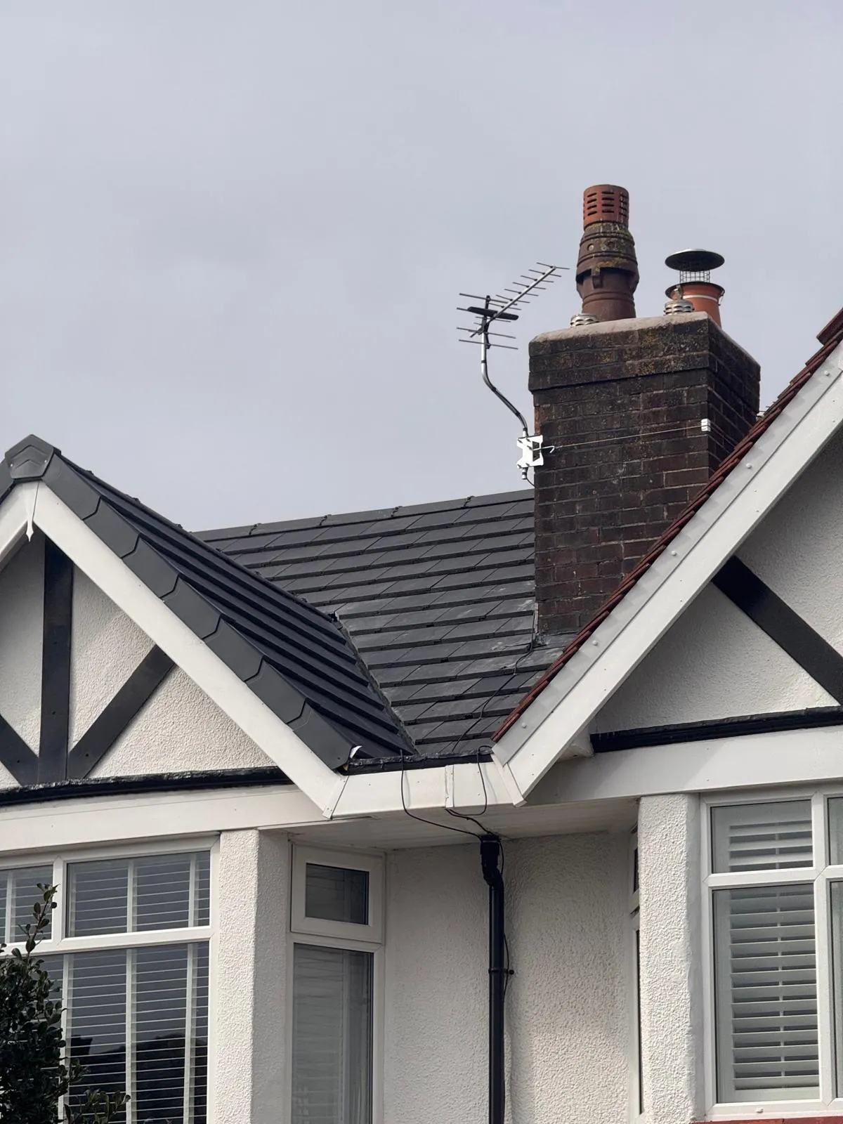 Residential pitched roof with dark grey tiles, white fascias and soffits, and a brick chimney.