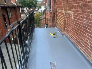 Newly installed grey flat roof, possibly EPDM or GRP, on a residential property with a metal railing and brick wall.