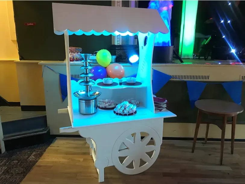 White candy cart with chocolate fountain, marshmallows, and other sweets at an event
