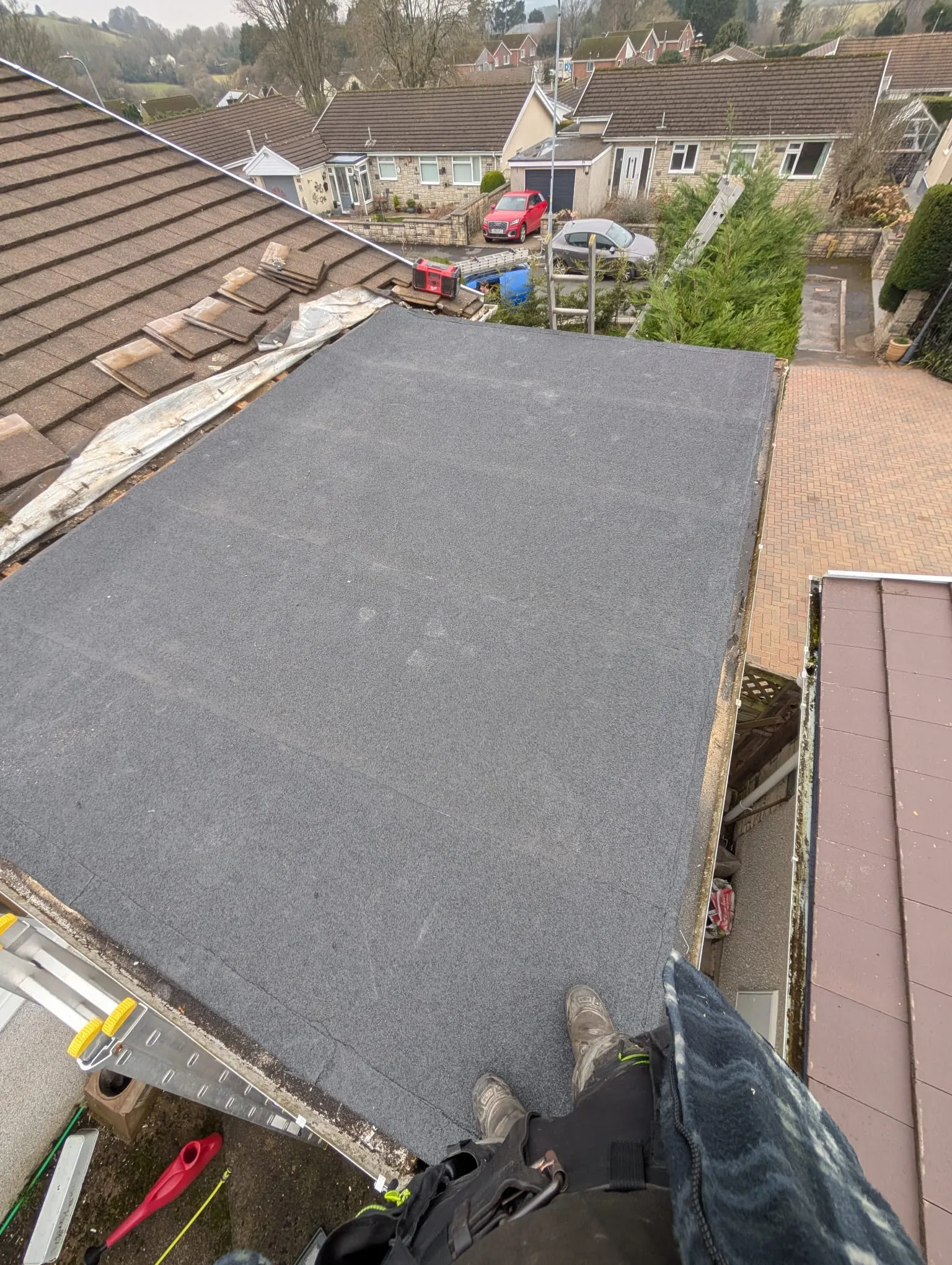 Newly installed dark grey flat roof on a residential building, seen from a roofer's perspective.