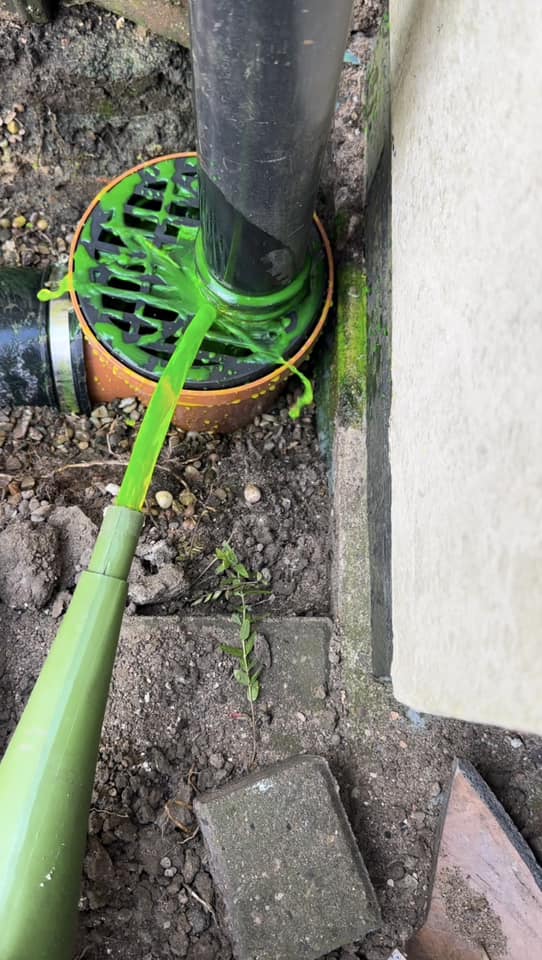 Green dye overflowing from a blocked outdoor drain gully