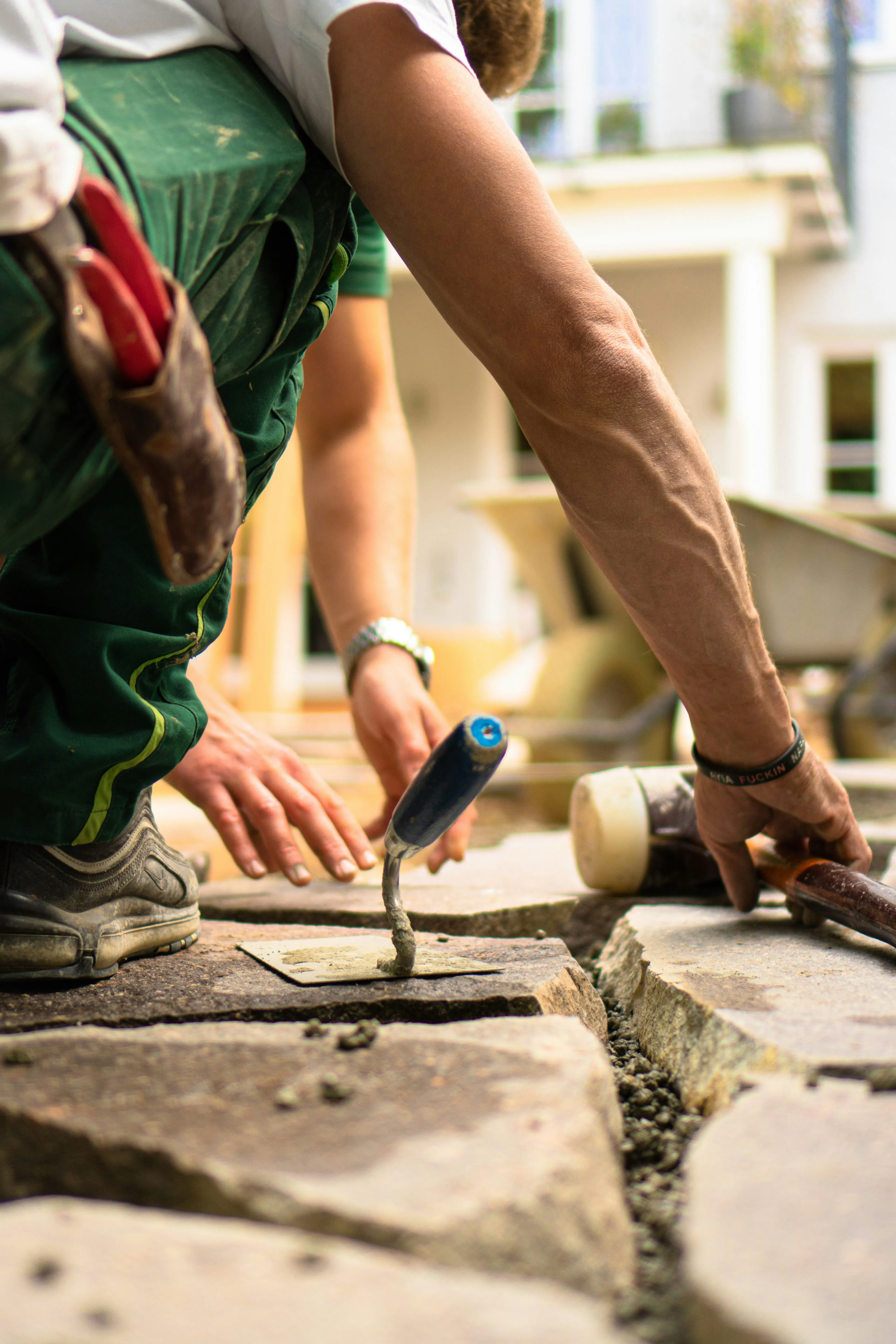 Close-up of a paver using a trowel to carefully lay large stone paving slabs during installation.