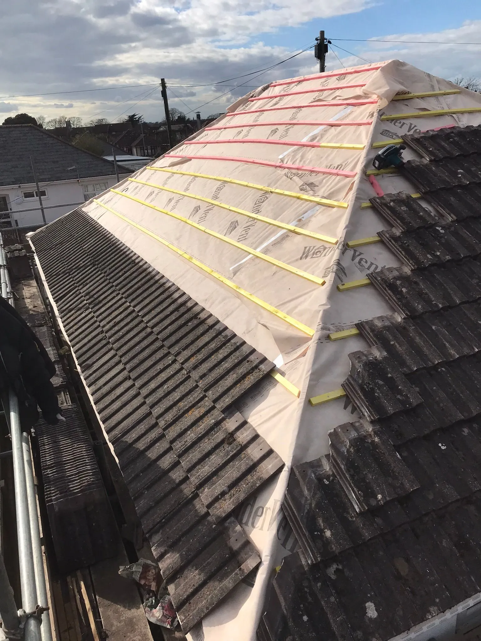 Residential pitched roof partially stripped and re-battened for new tiles, with scaffolding visible.