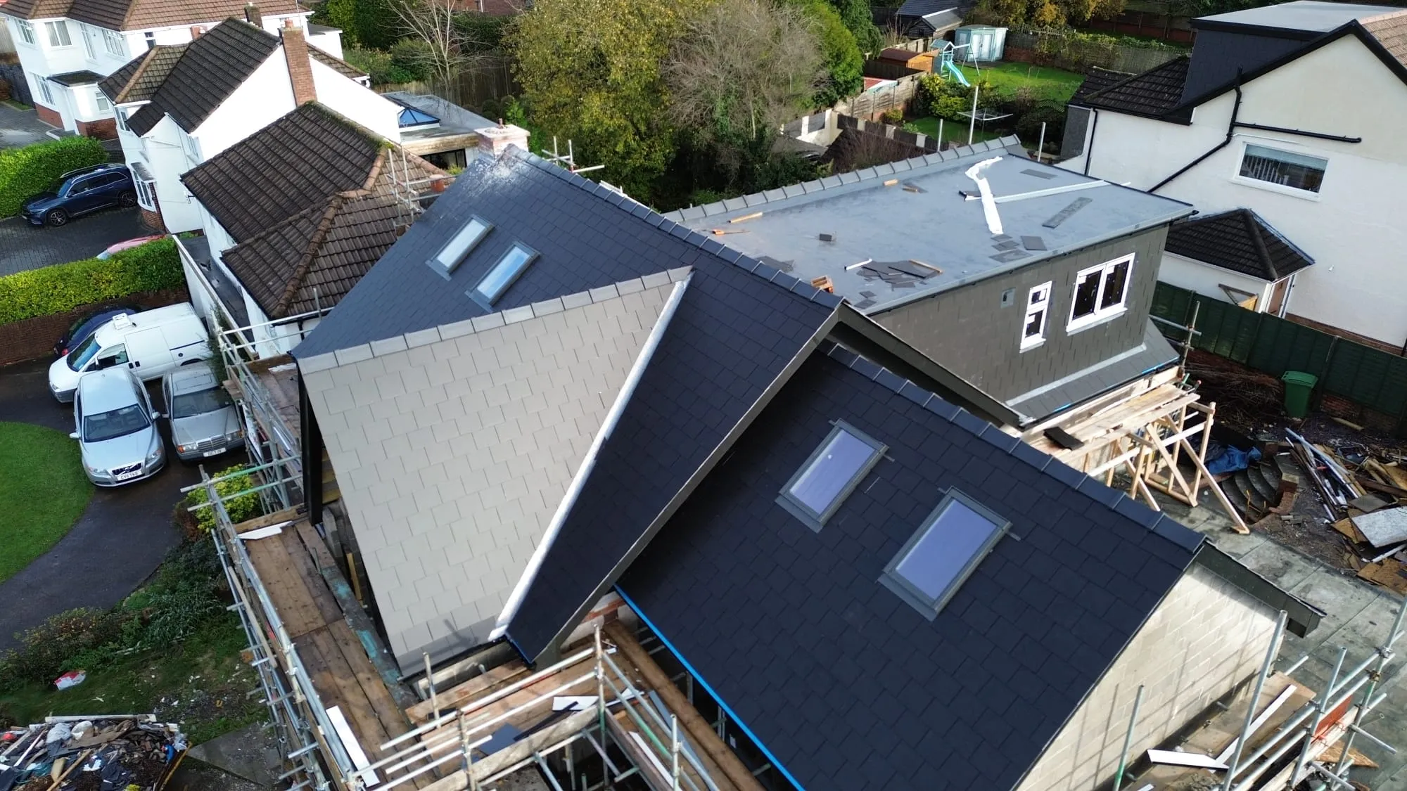 Aerial view of a new roof being installed on a house, featuring dark grey and light grey tiles, Velux windows, and a flat roof section.